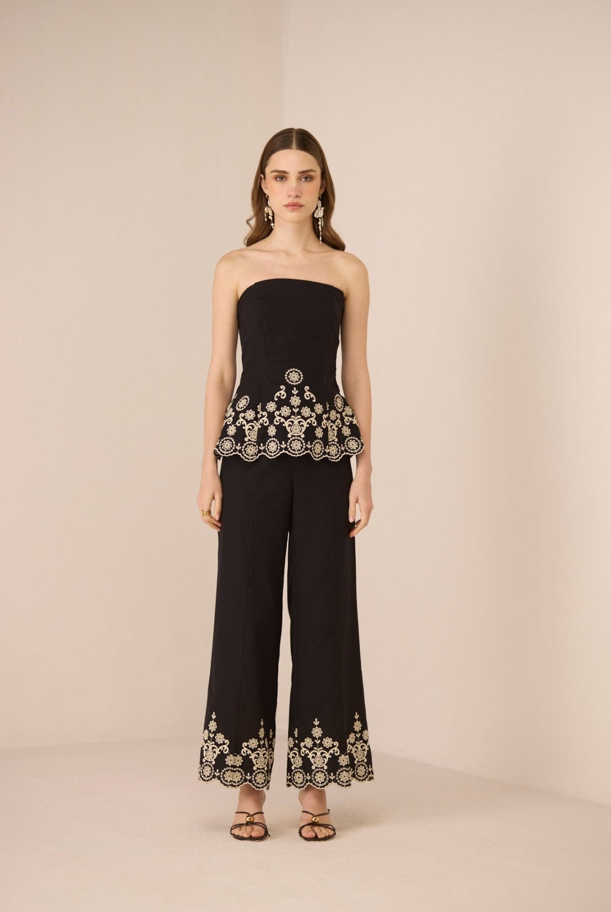 Woman wearing a black strapless top and wide-leg pants with embroidery on a beige background Calling June