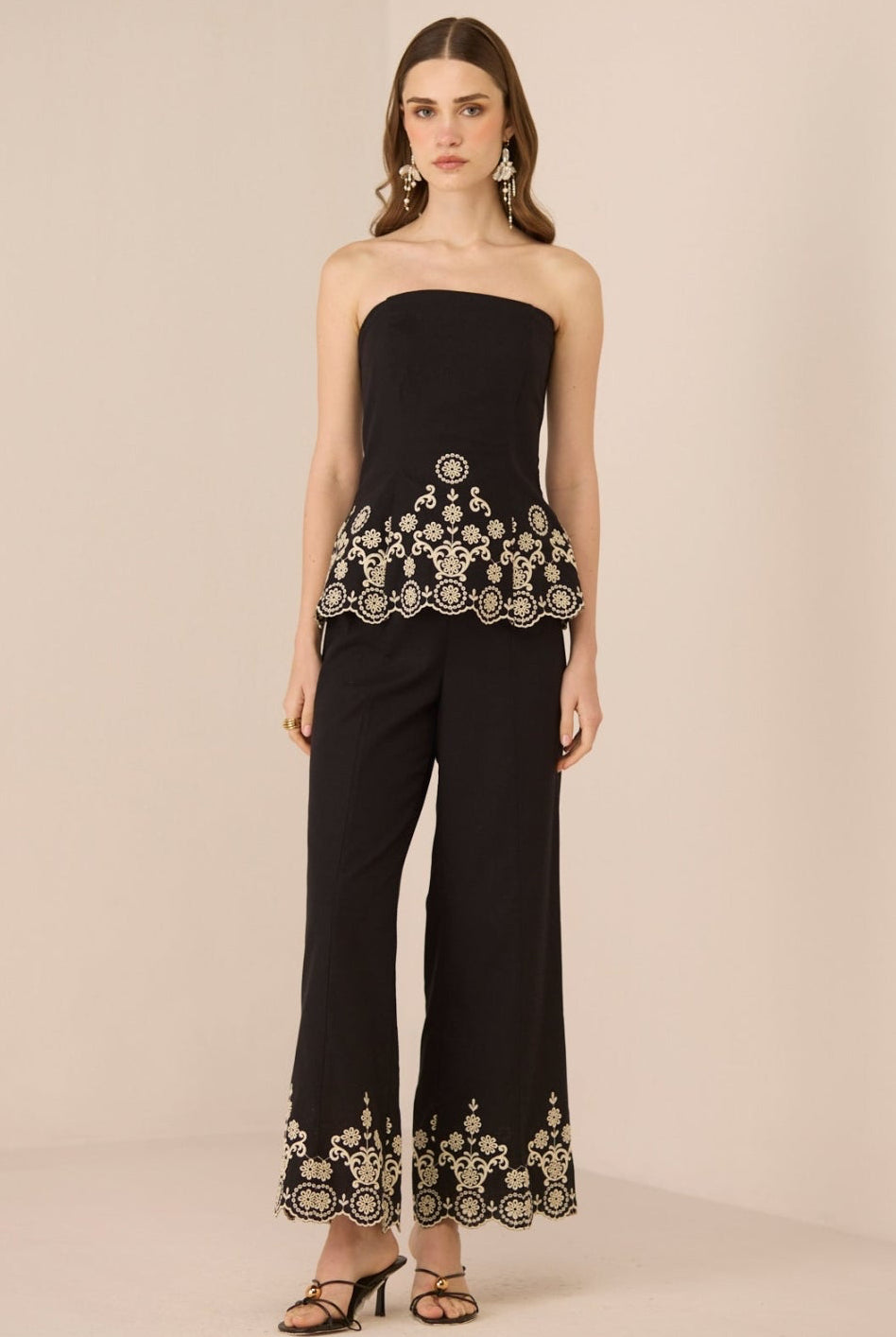 Woman wearing a black strapless top and pants with embroidery on a beige background Calling June