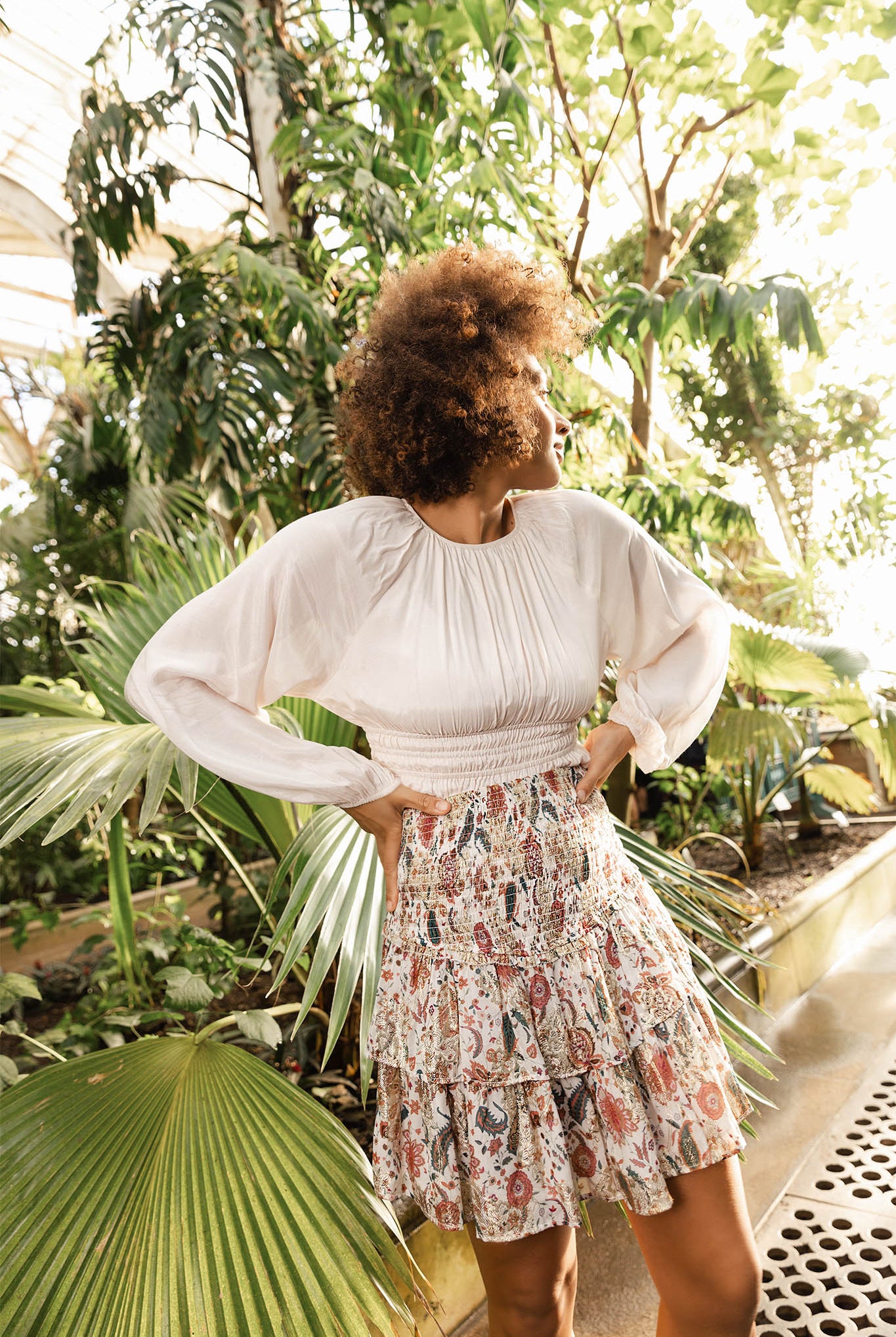 Woman standing in a lush, green outdoor setting with plants and trees Calling June