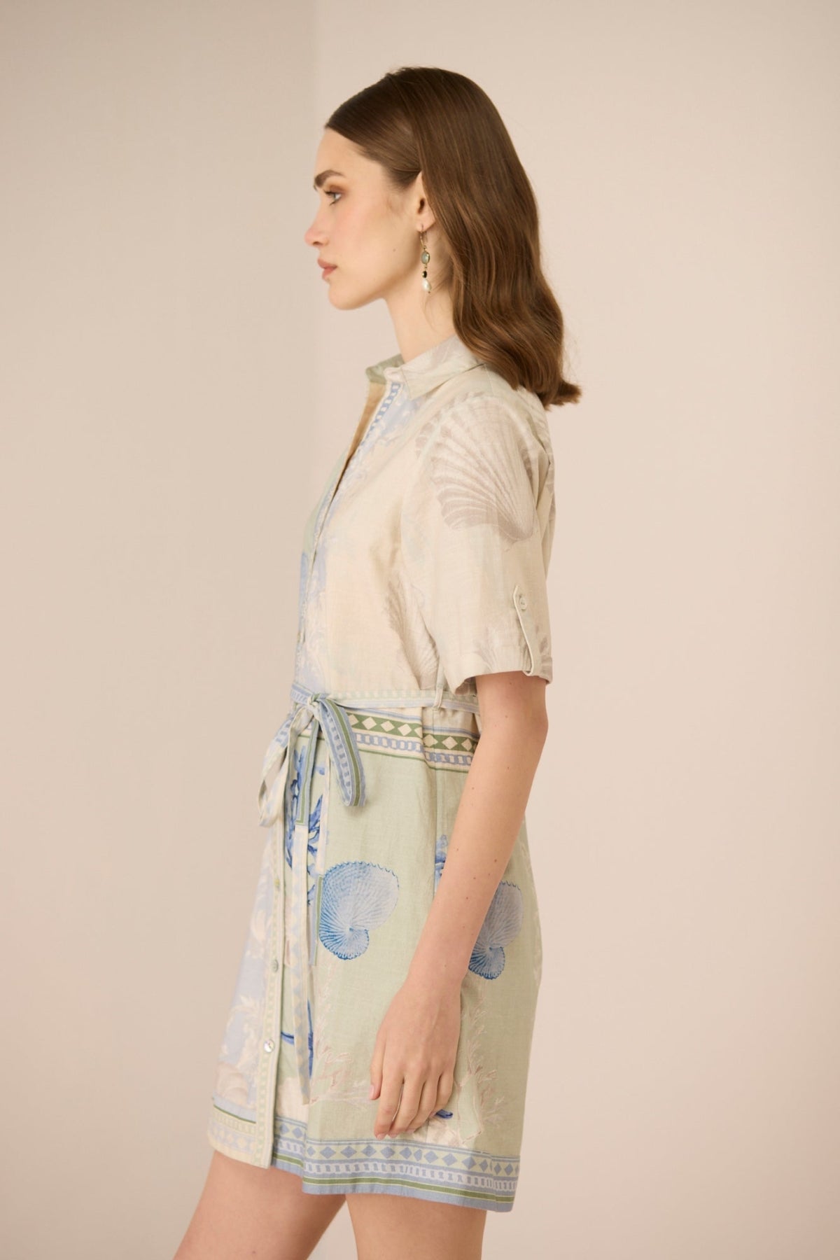 Woman wearing a light-colored dress with a patterned belt against a beige background Calling June
