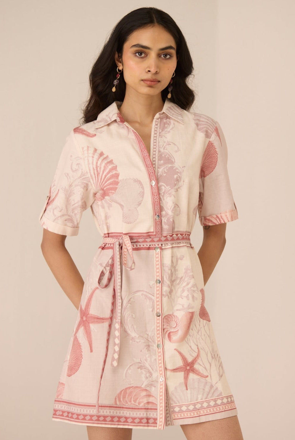 Woman wearing a pink and white dress with shell pattern on a beige background Calling June