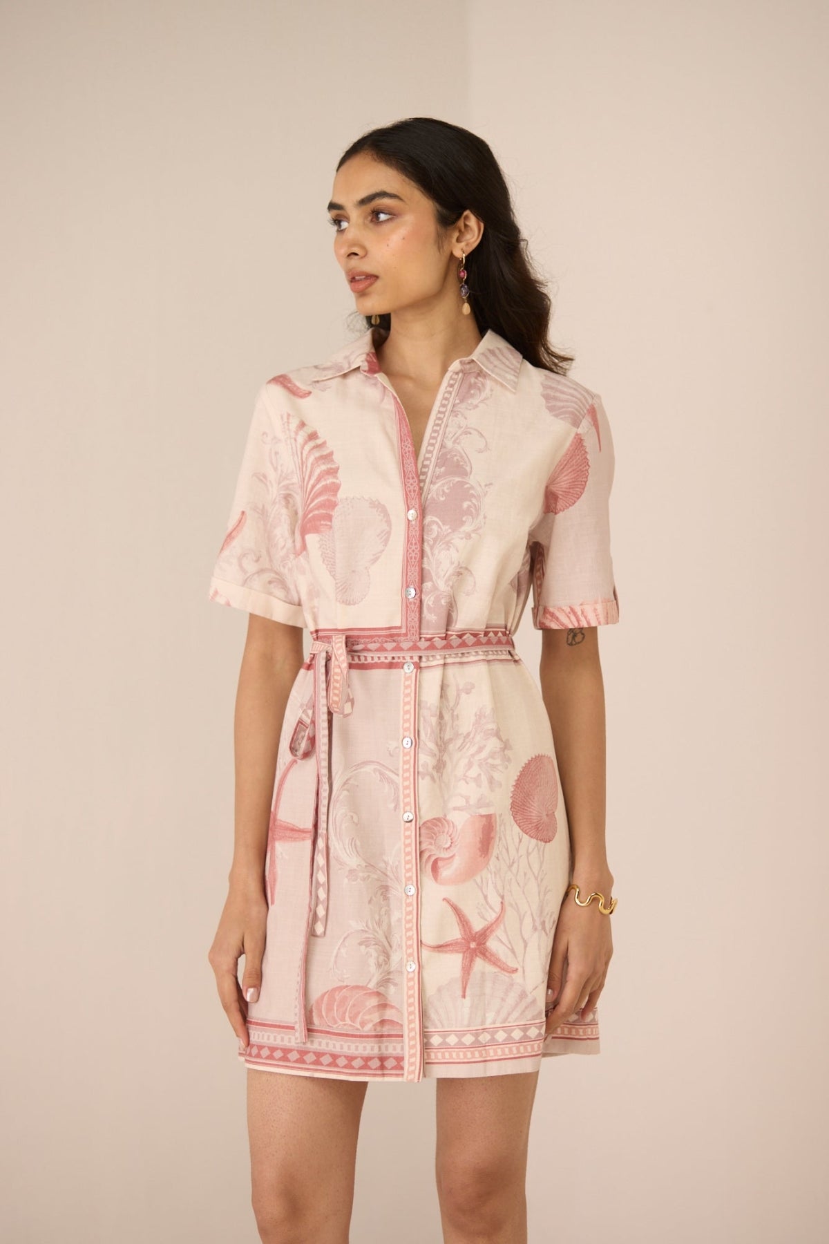Woman wearing a pink dress with shell pattern against a beige background Calling June