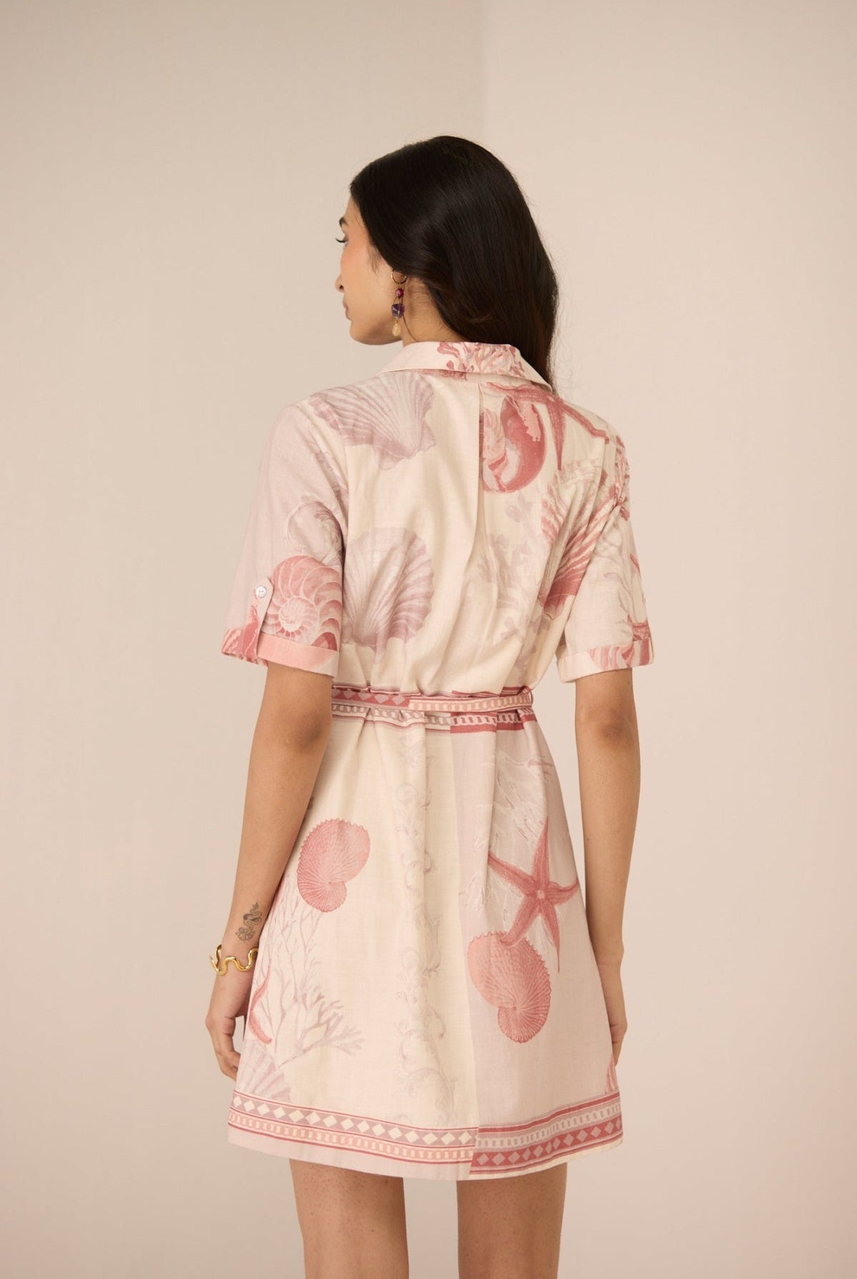 Woman wearing a light-colored dress with pink floral patterns on a plain background Calling June