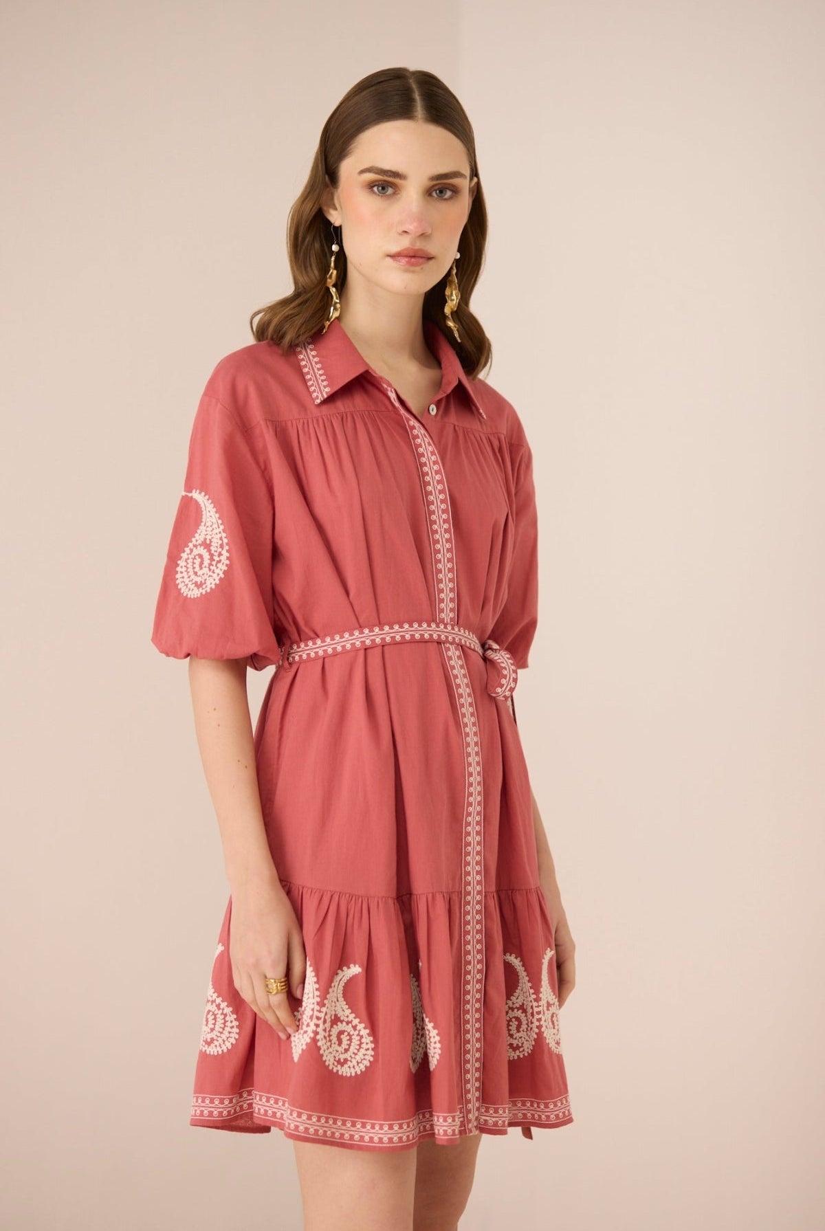 Woman wearing a pink dress with white embroidery on a beige background Calling June