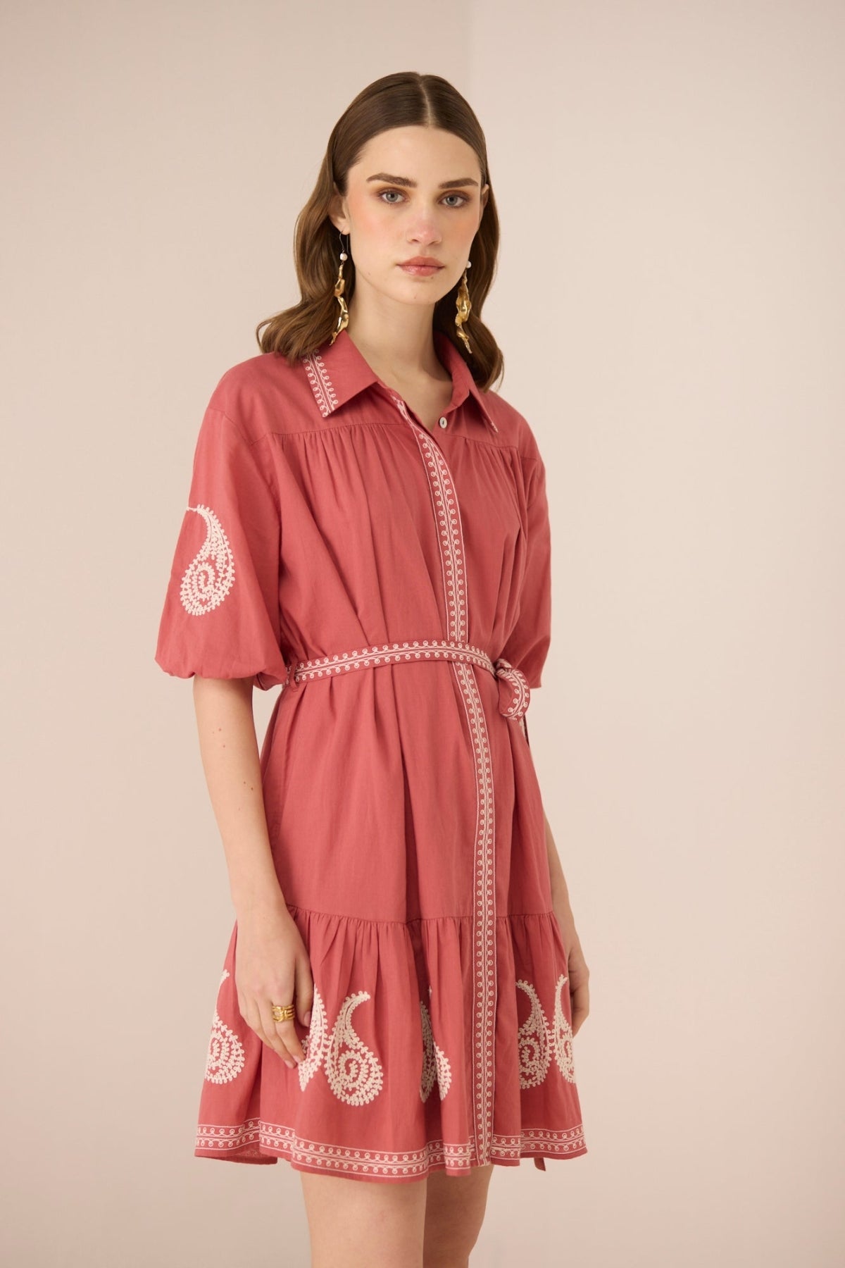 Woman wearing a pink dress with white embroidery on a beige background Calling June