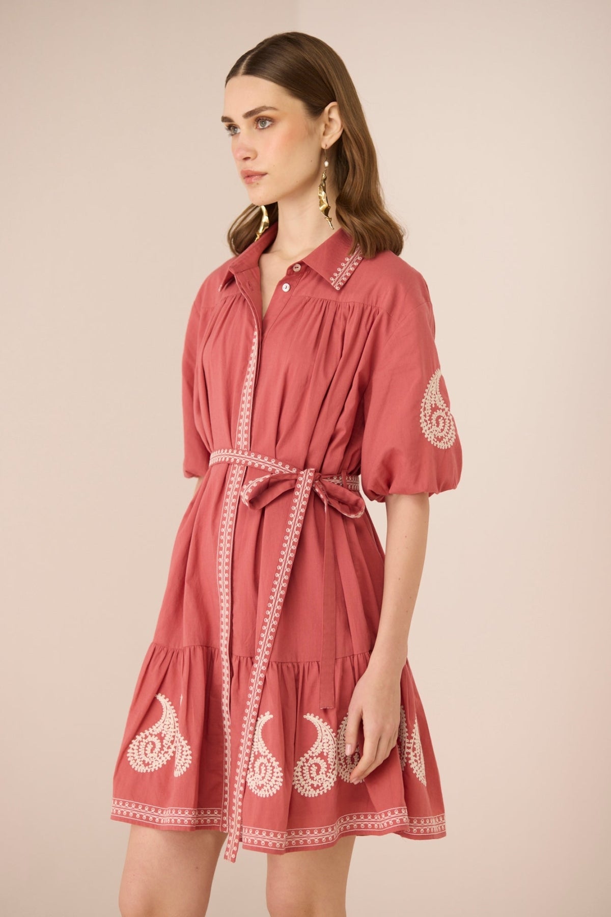 Woman wearing a red dress with white embroidery on a beige background Calling June