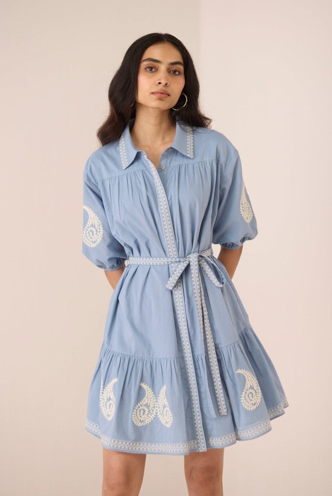 Woman wearing a blue dress with white embroidery on a beige background Calling June