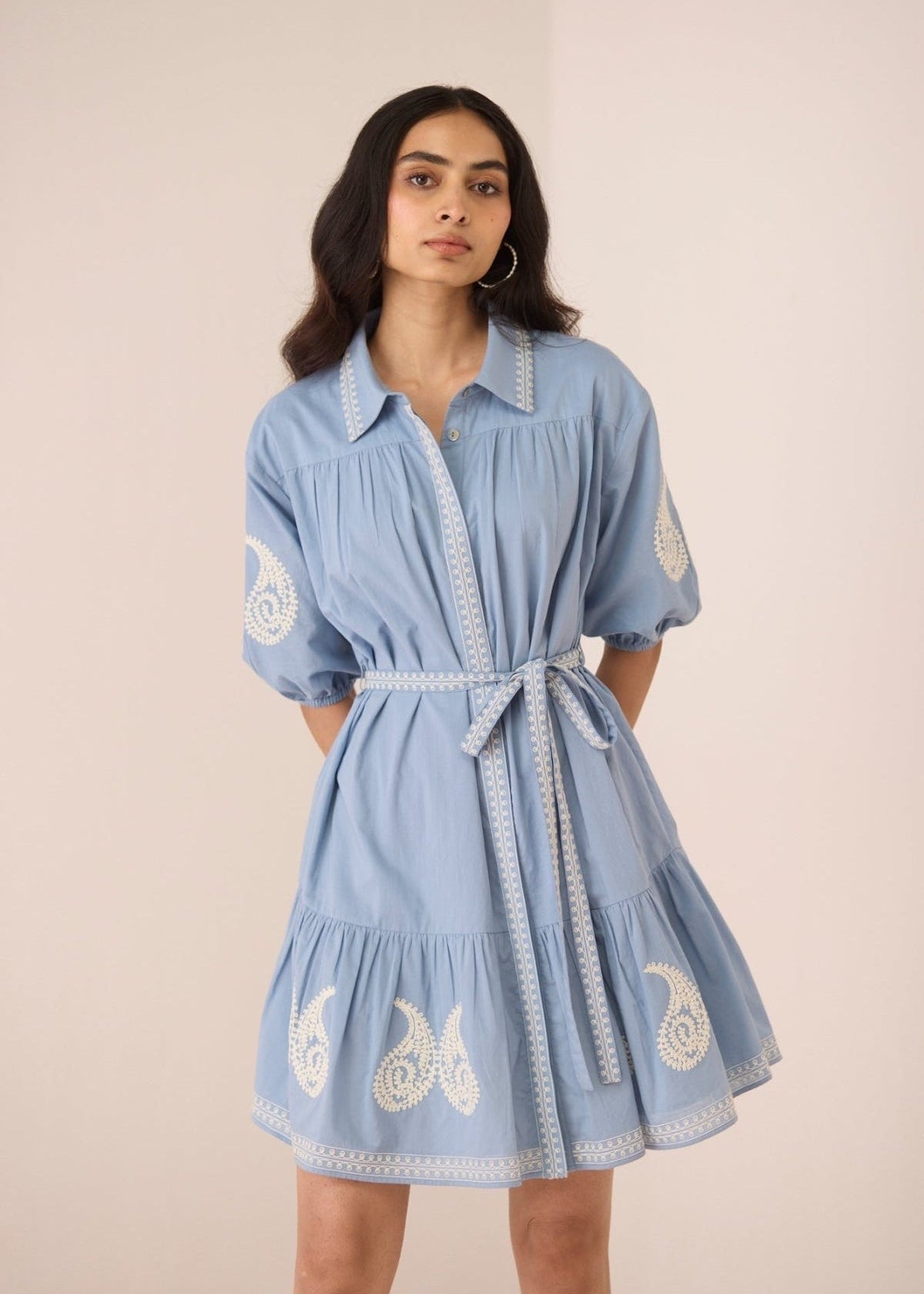Woman wearing a blue dress with white embroidery on a beige background Calling June