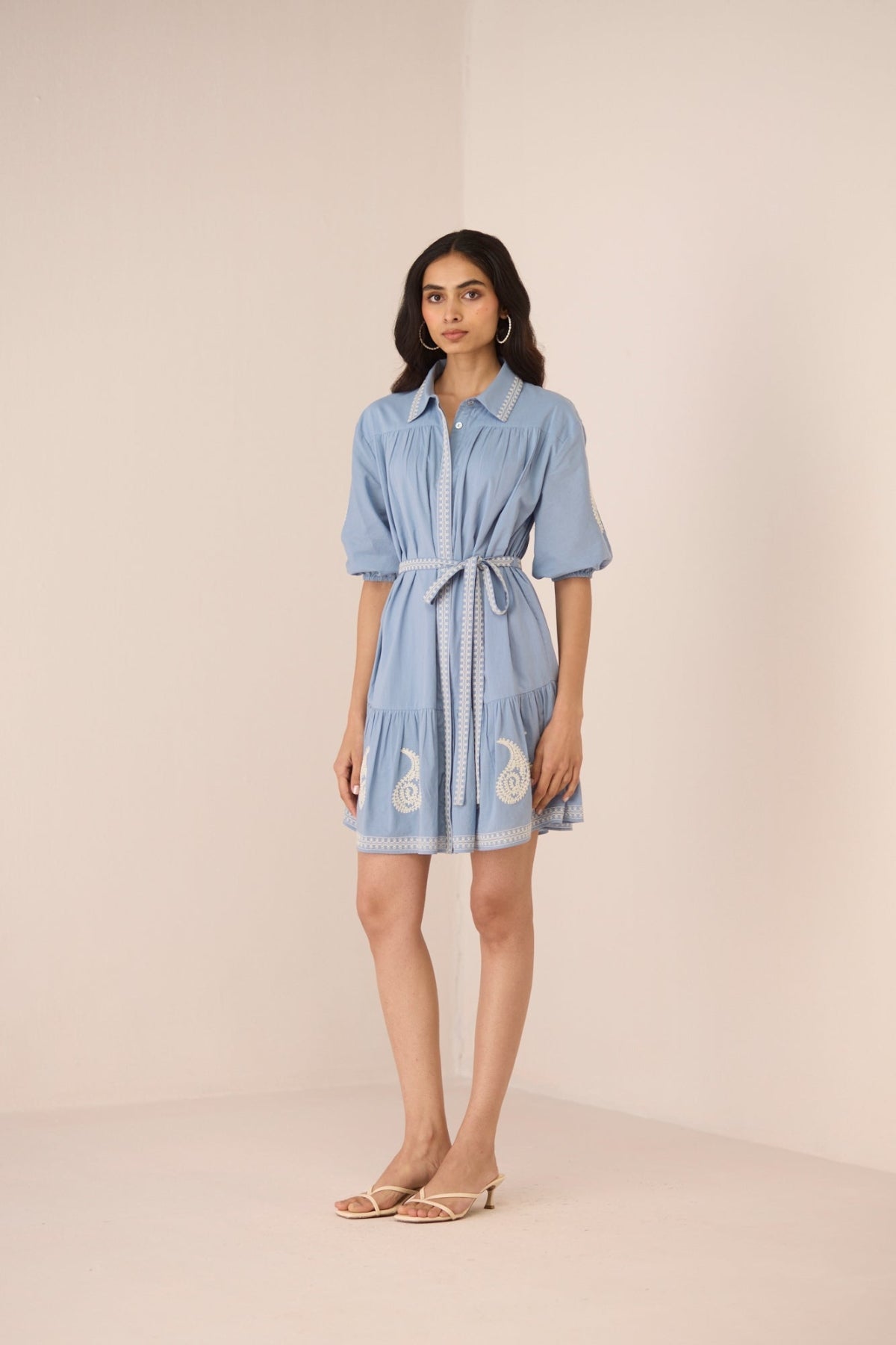 Woman wearing a light blue dress with a belt on a beige background Calling June