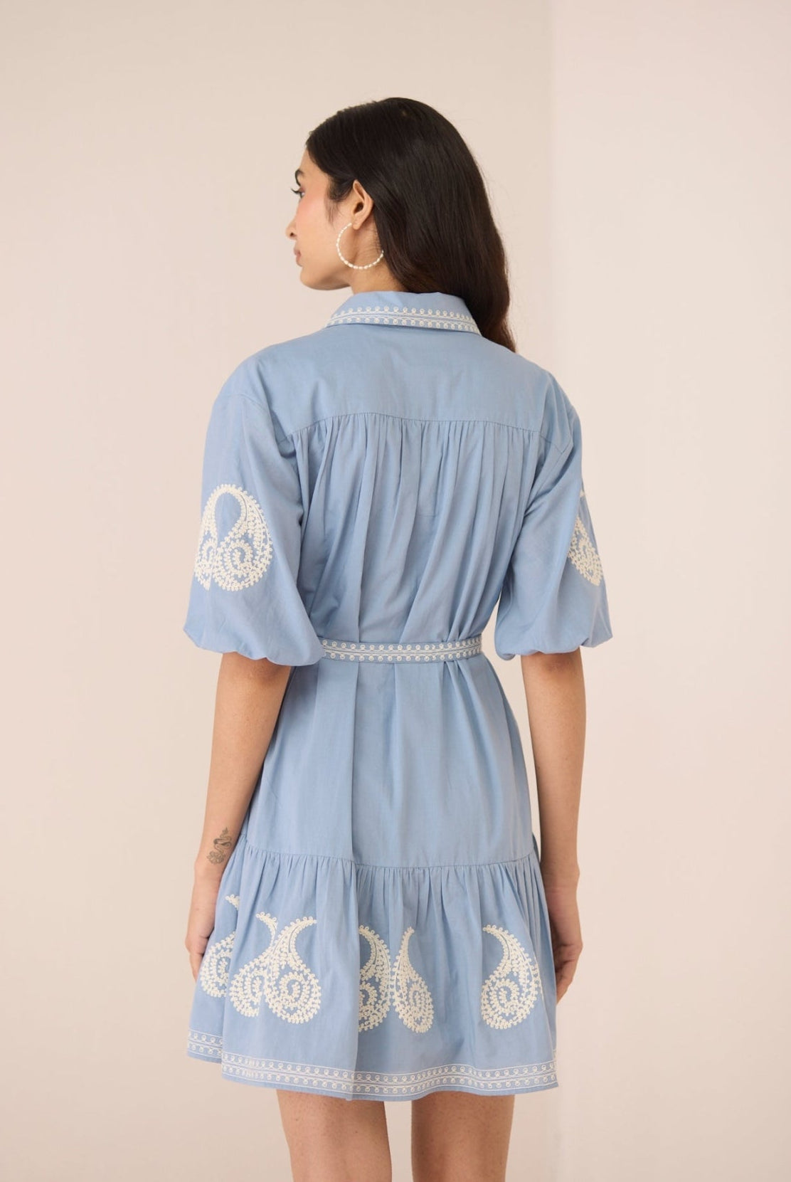 Woman wearing a blue dress with white embroidery on a beige background Calling June
