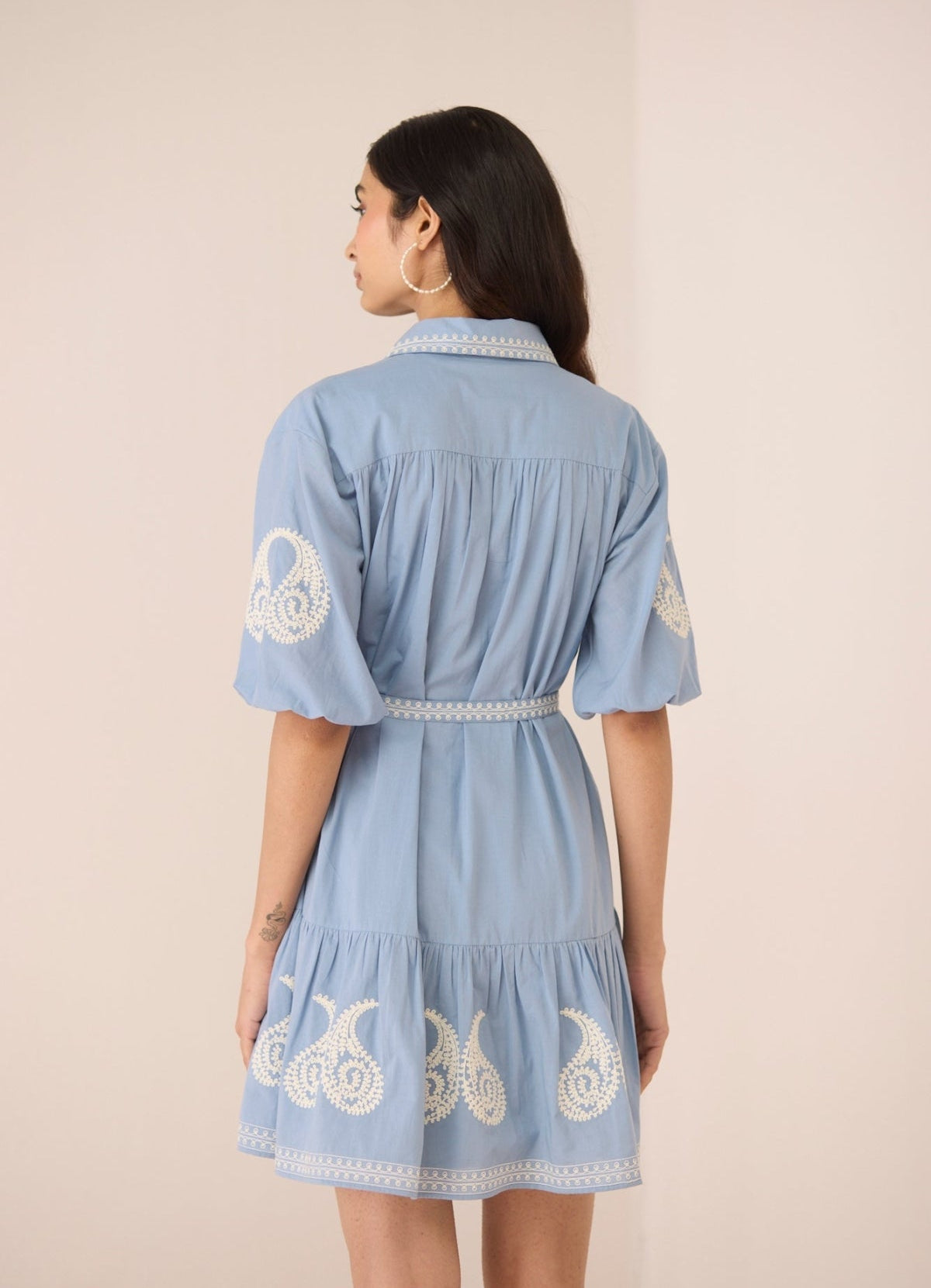 Woman wearing a blue dress with white embroidery on a beige background Calling June