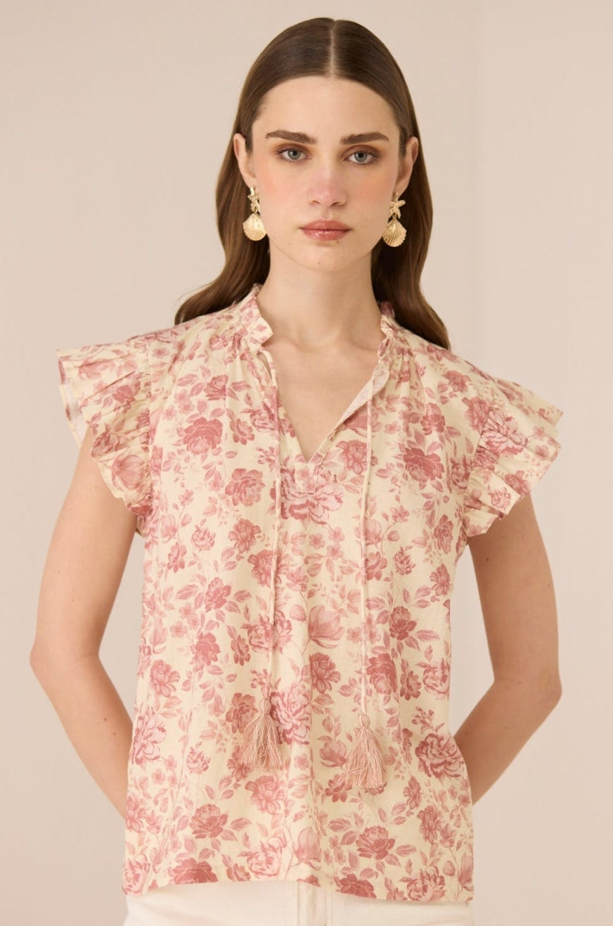 Woman wearing a floral blouse with ruffled sleeves against a beige background Calling June