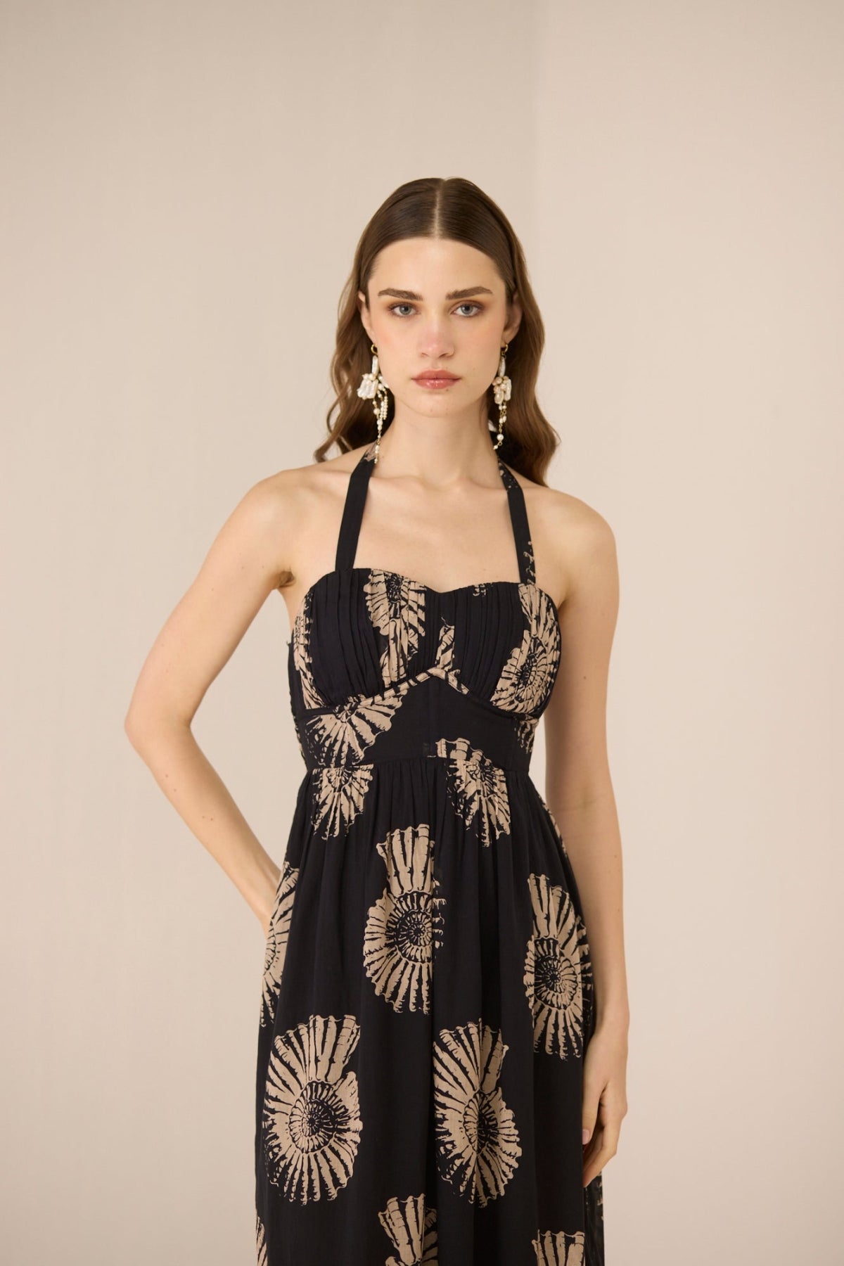 Woman wearing a black dress with gold floral patterns on a beige background Calling June