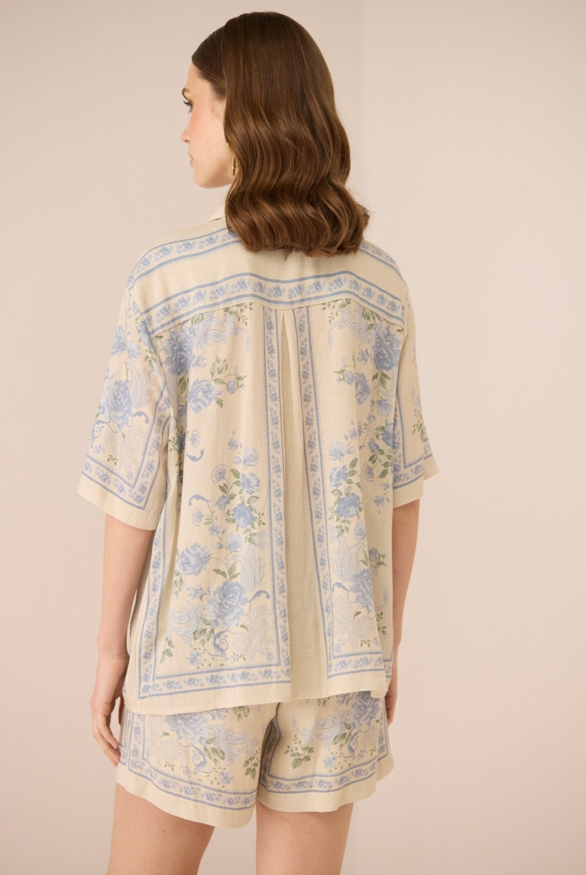 Woman wearing a beige outfit with floral patterns on a plain background Calling June