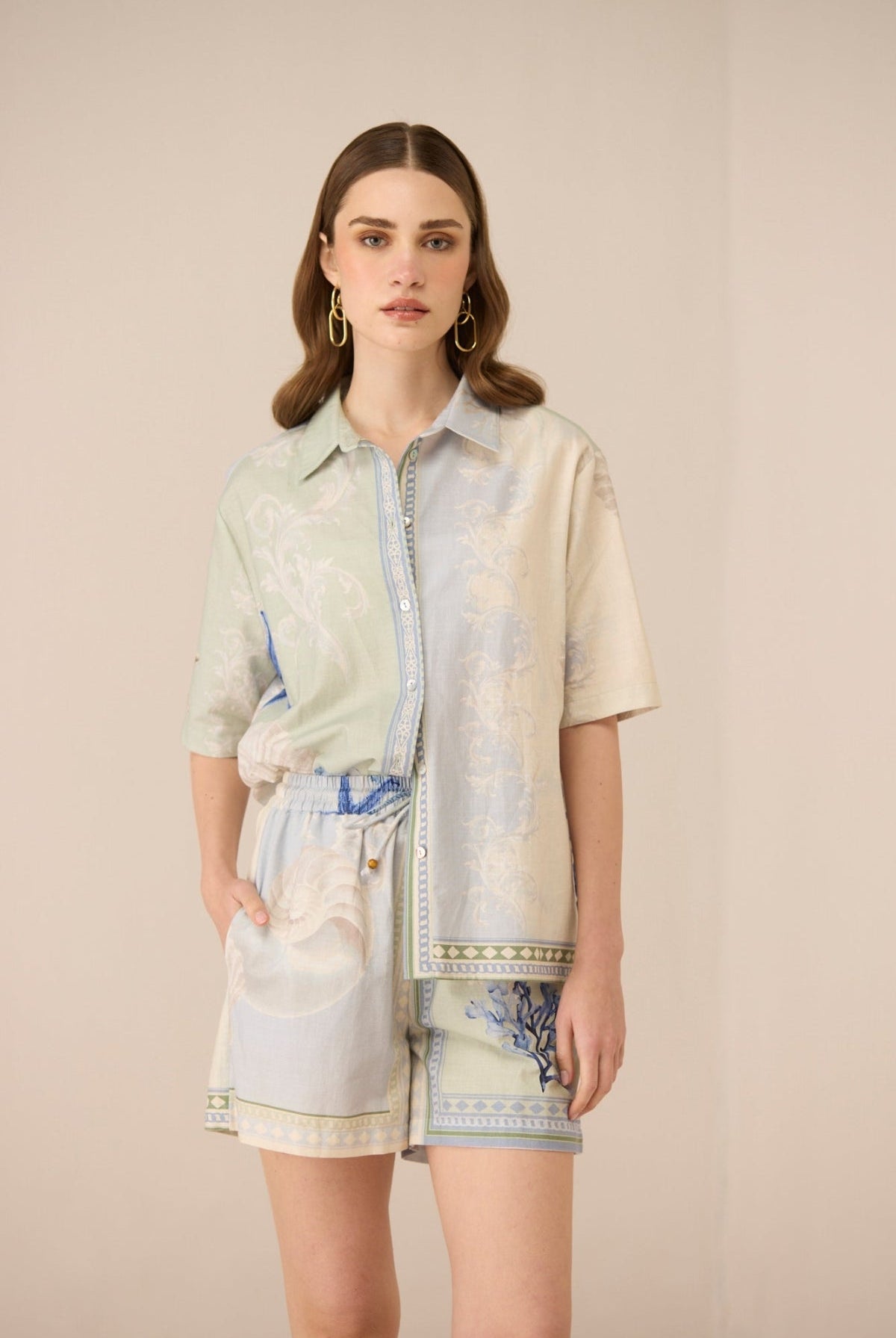 Woman wearing a light-colored shirt with a patterned skirt against a plain background Calling June