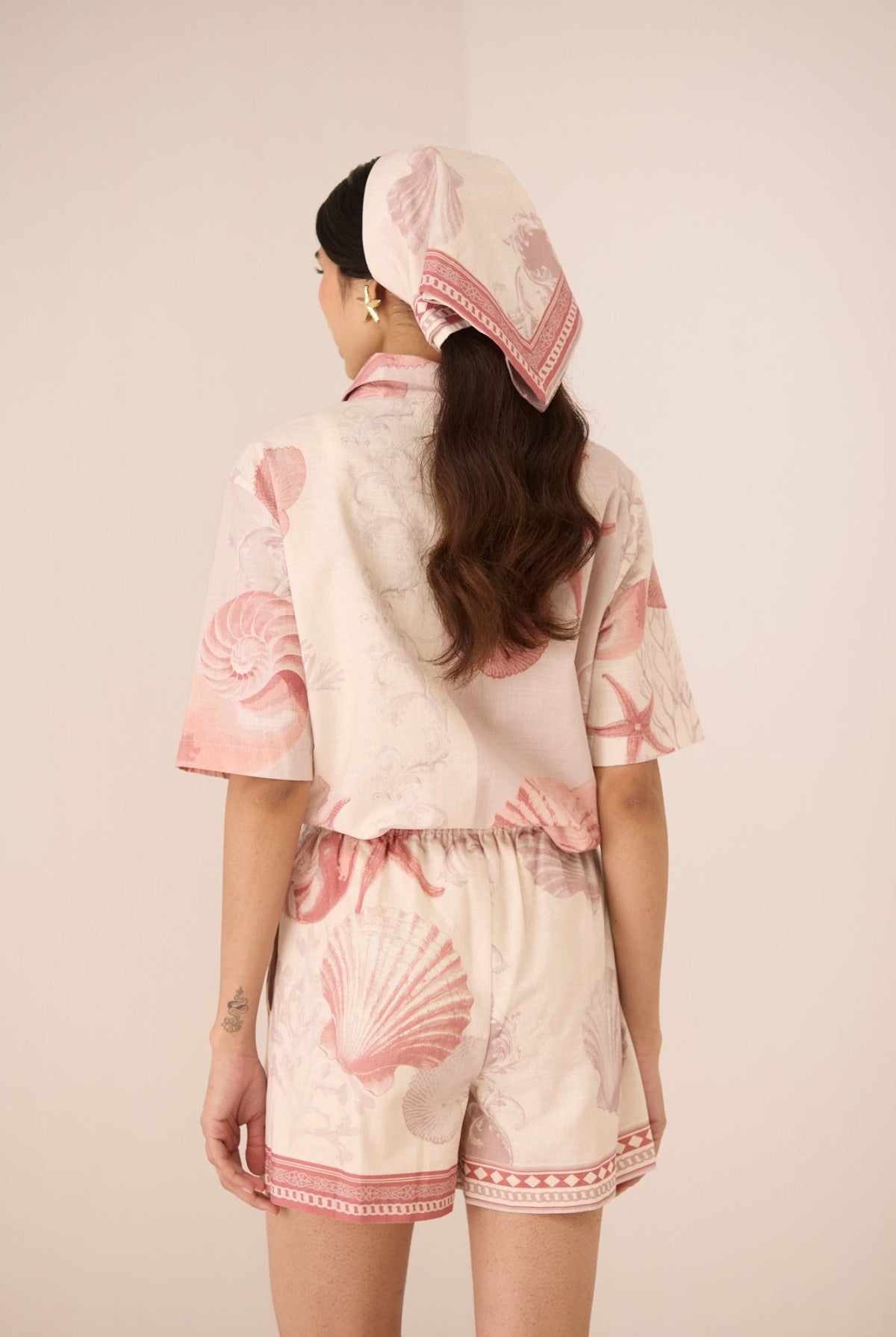 Woman wearing a pink and white outfit with shell patterns on a beige background Calling June