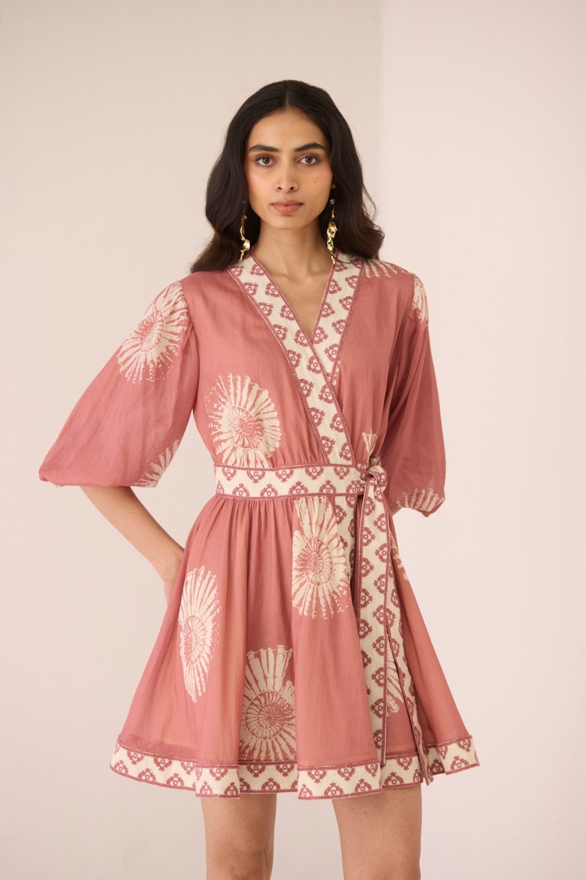 Woman wearing a pink patterned dress against a plain background Calling June