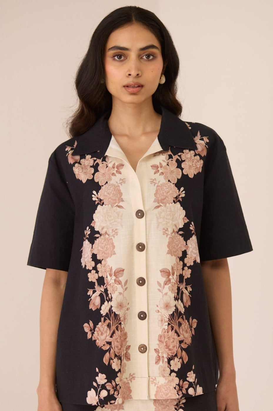 Woman wearing a black floral jacket over a cream shirt with matching pants on a beige background Calling June