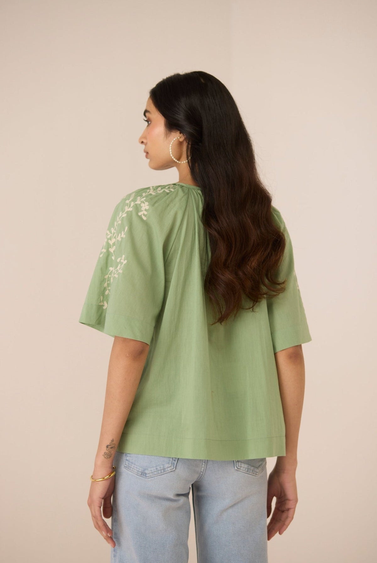 Woman wearing a green top with floral embroidery on a beige background Calling June