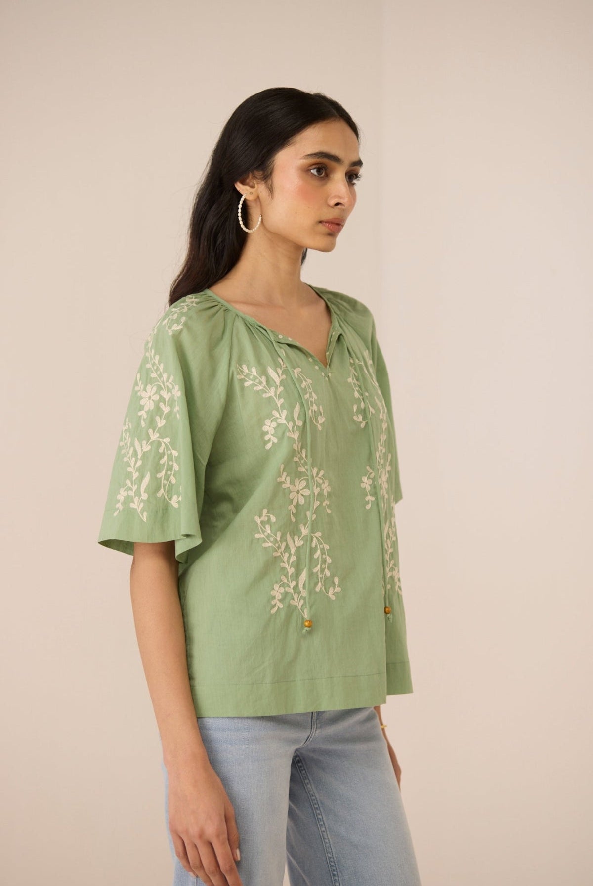 Woman wearing a green embroidered blouse against a beige background Calling June