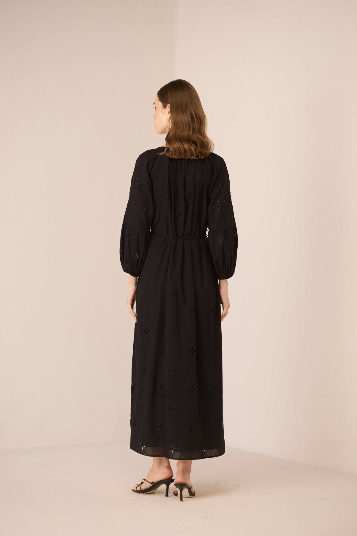 Woman wearing a black dress with long sleeves and a belt, standing against a plain background. Calling June