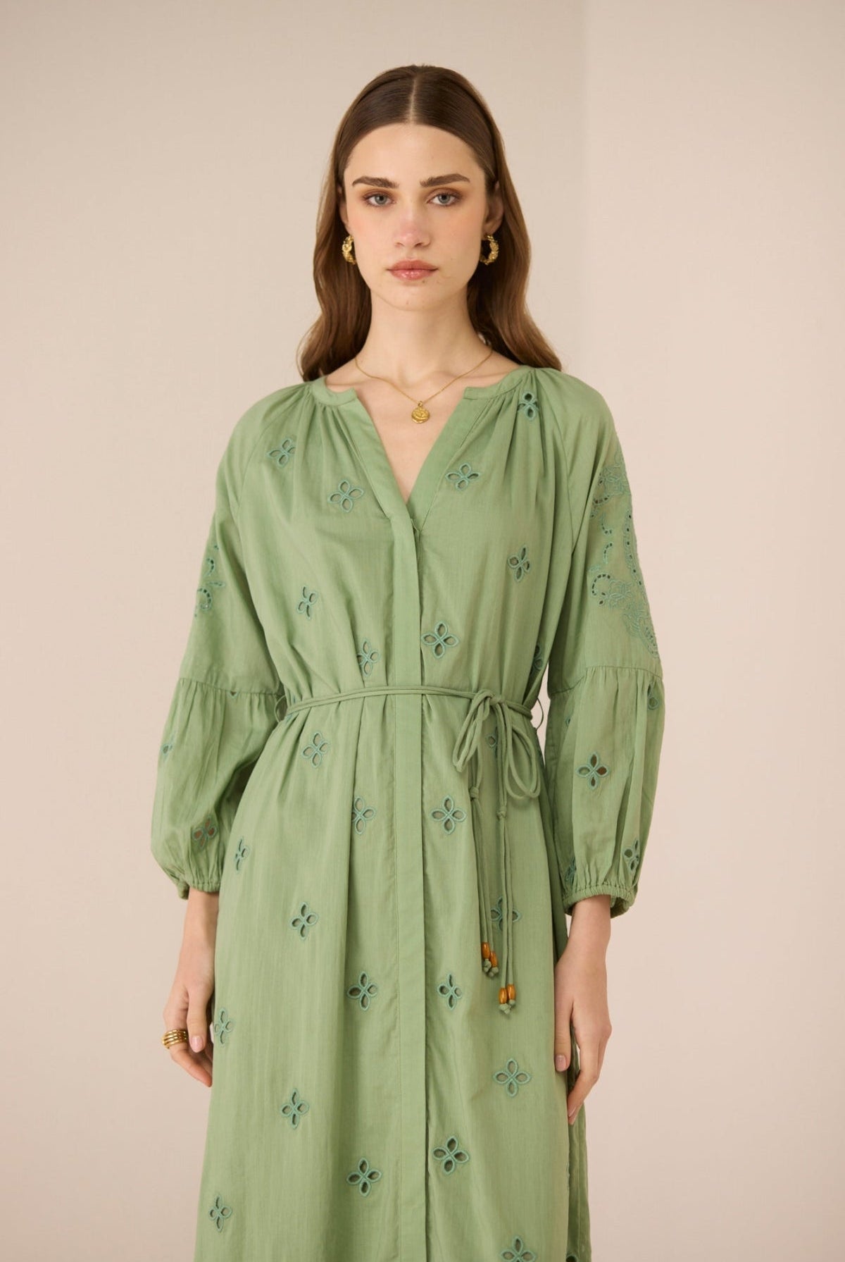 Woman wearing a green dress with floral embroidery against a beige background Calling June