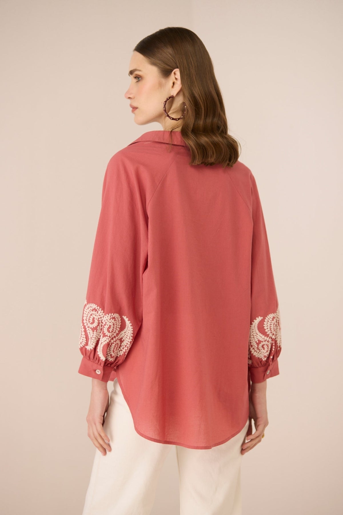 Woman wearing a pink blouse with lace details on sleeves against a beige background Calling June