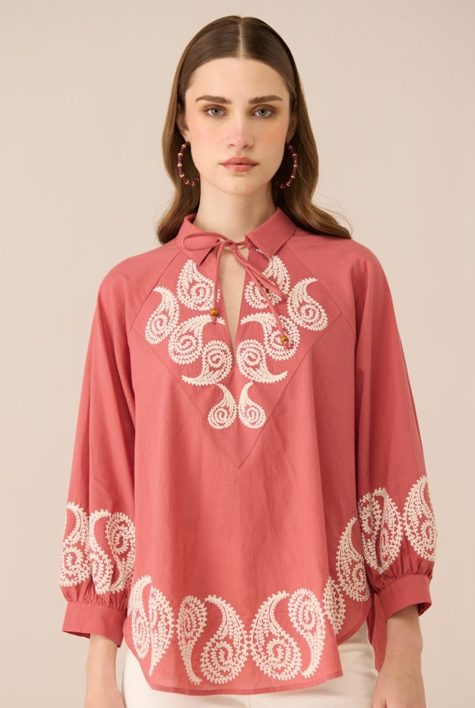 Woman wearing a red blouse with white embroidery on a beige background Calling June