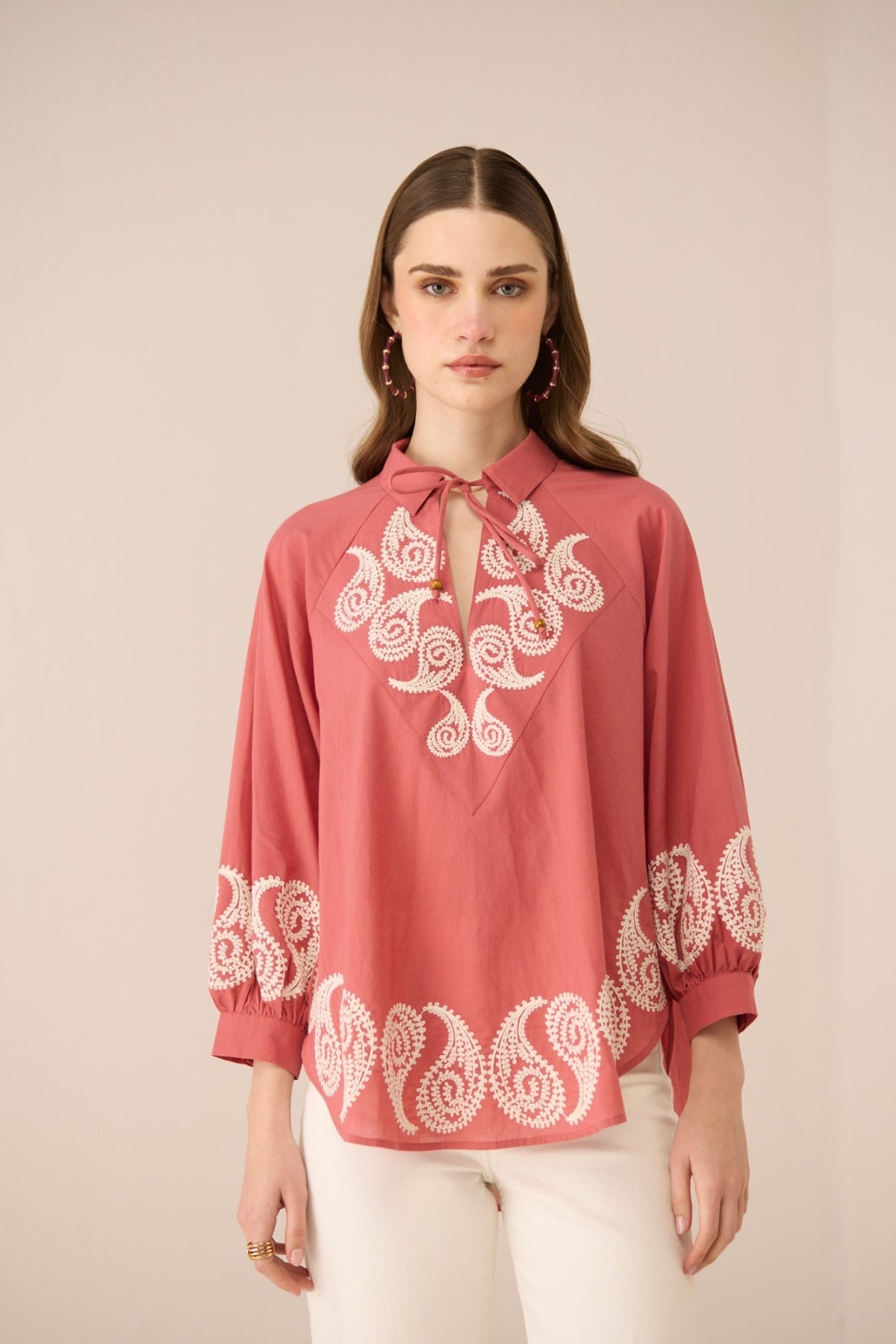 Woman wearing a red blouse with white embroidery on a beige background Calling June