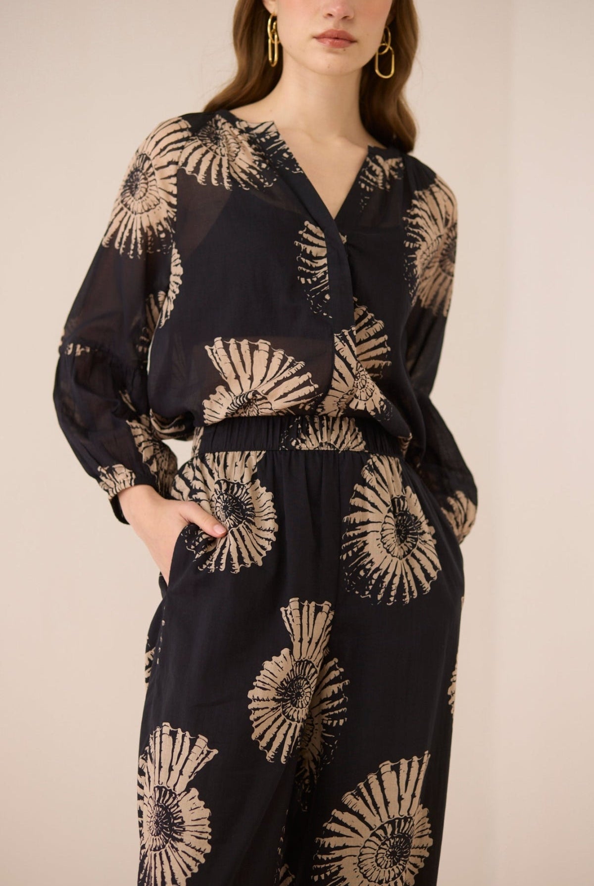 Woman wearing a black outfit with gold floral patterns on a beige background Calling June