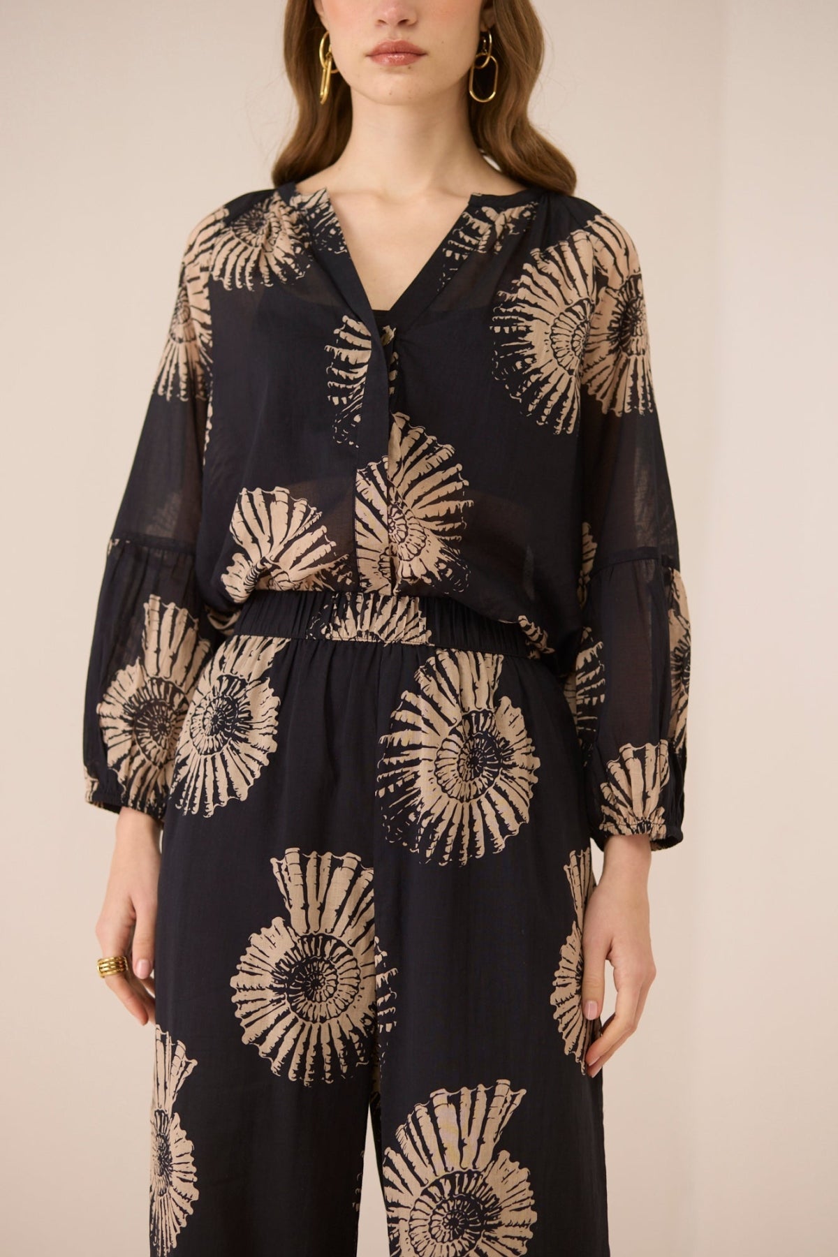 Woman wearing a black outfit with beige floral patterns on a beige background Calling June