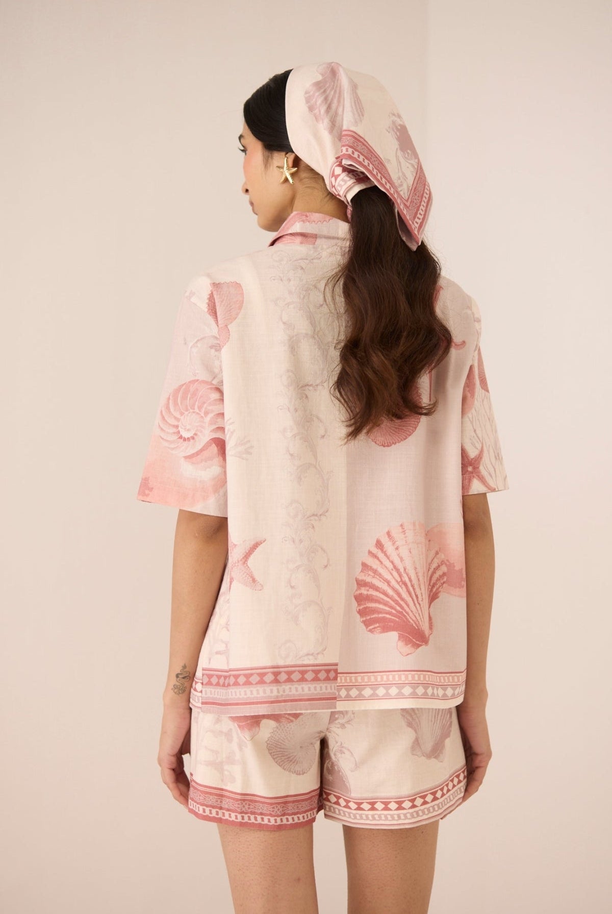 Woman wearing a matching top and shorts set with pink shell patterns on a beige background Calling June