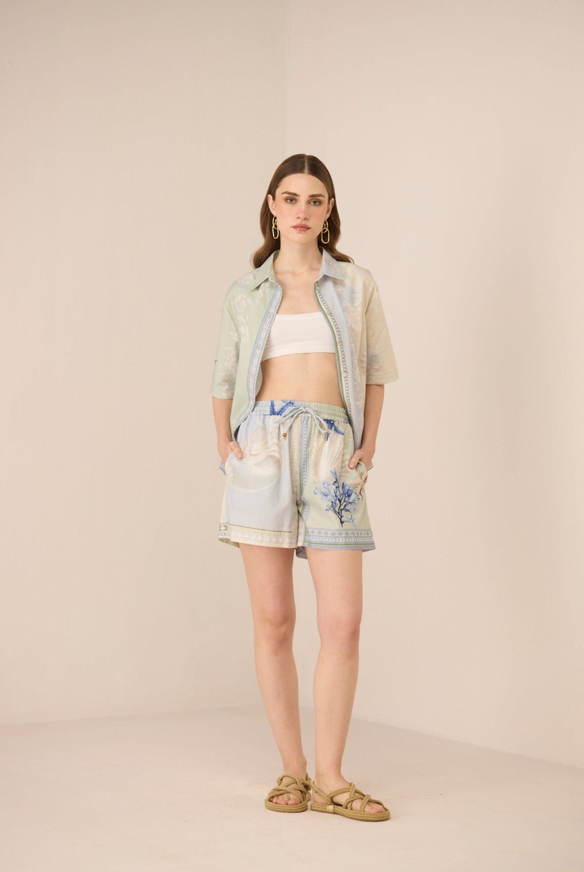 Woman wearing a light blue shirt, white top, and floral shorts on a beige background Calling June