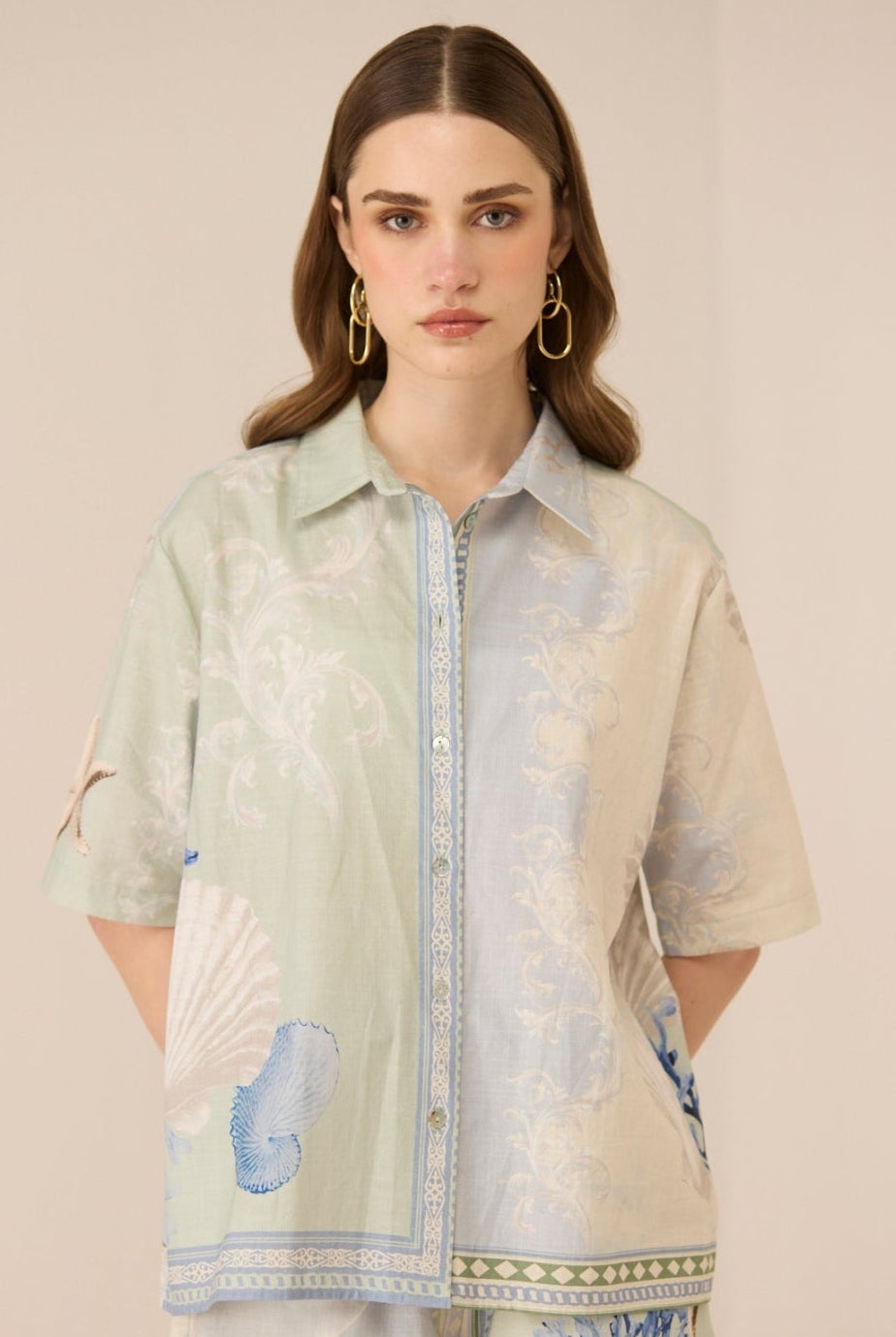 Woman wearing a light green and beige floral patterned shirt with matching shorts on a beige background Calling June