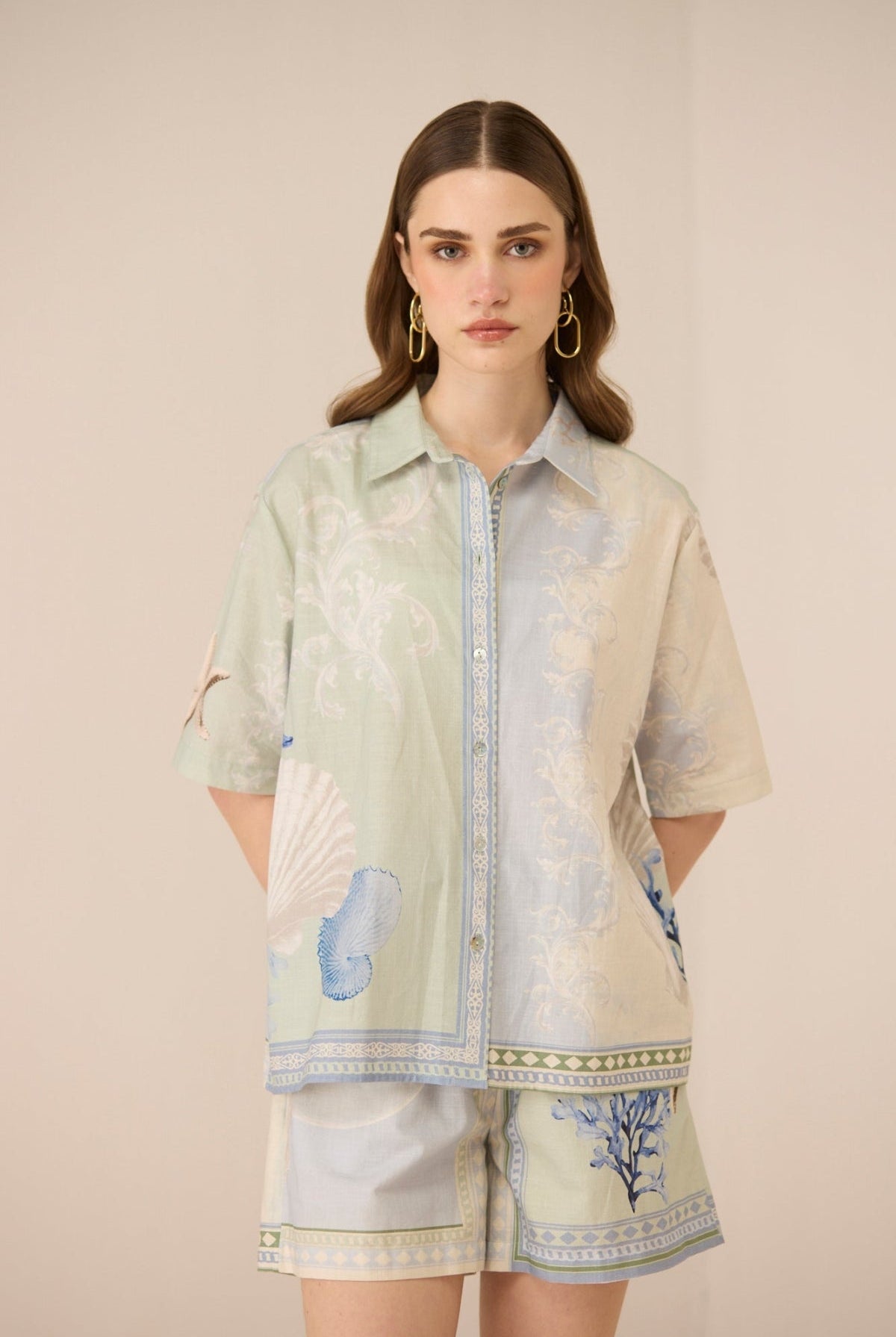 Woman wearing a light green and beige floral patterned shirt with matching shorts on a beige background Calling June