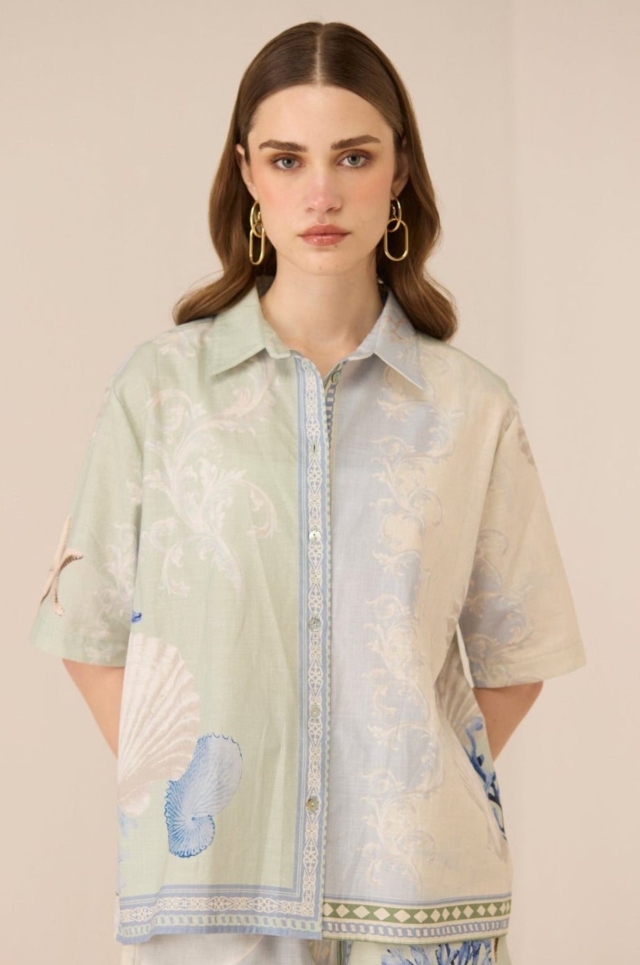 Woman wearing a light green and beige floral patterned shirt with matching shorts on a beige background Calling June