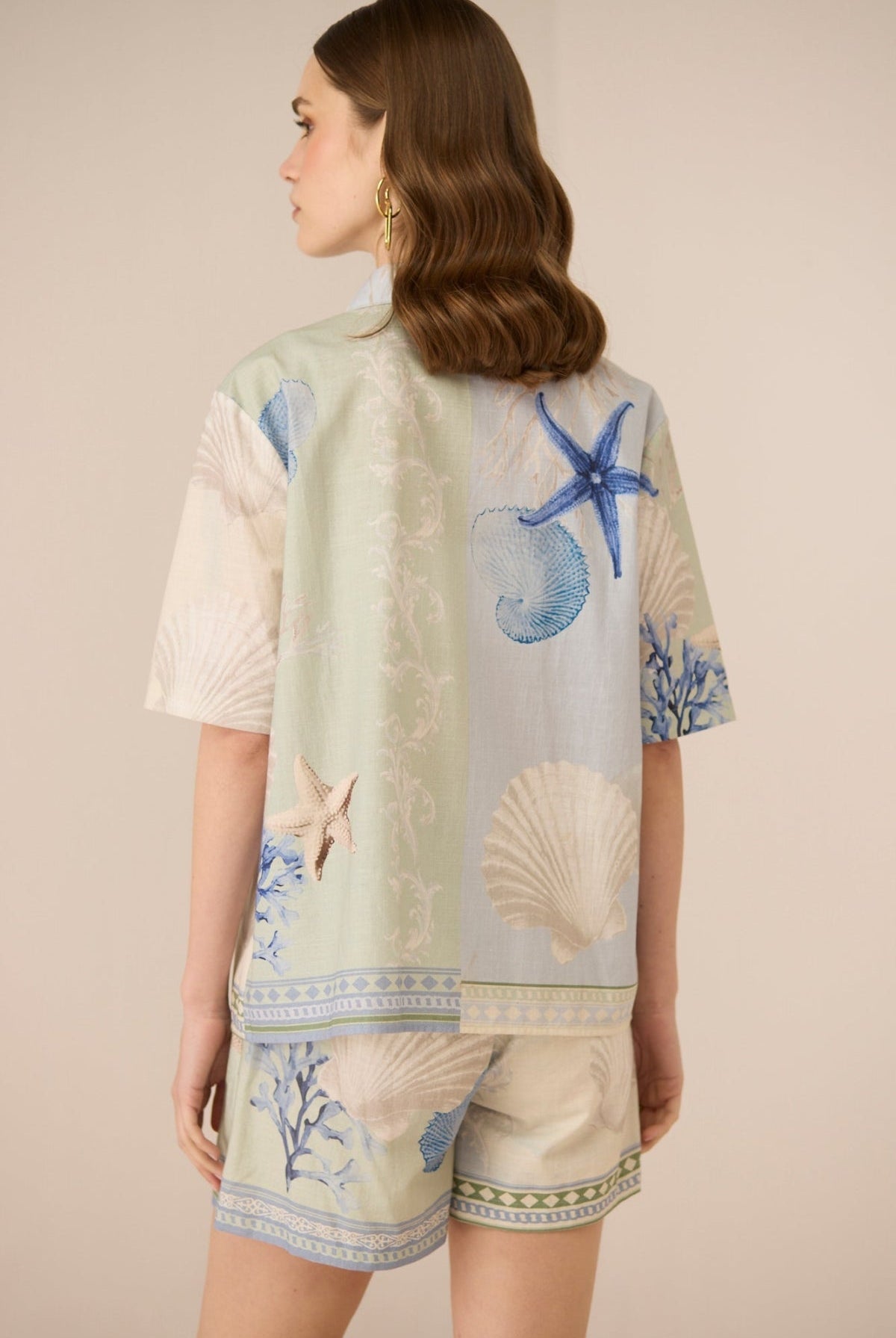 Woman wearing a short-sleeve top with marine-themed print on a beige background Calling June