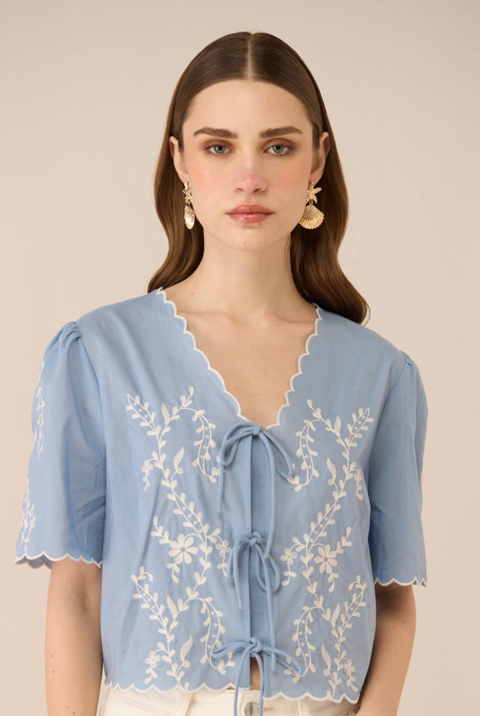 Woman wearing a light blue blouse with lace details on a beige background Calling June