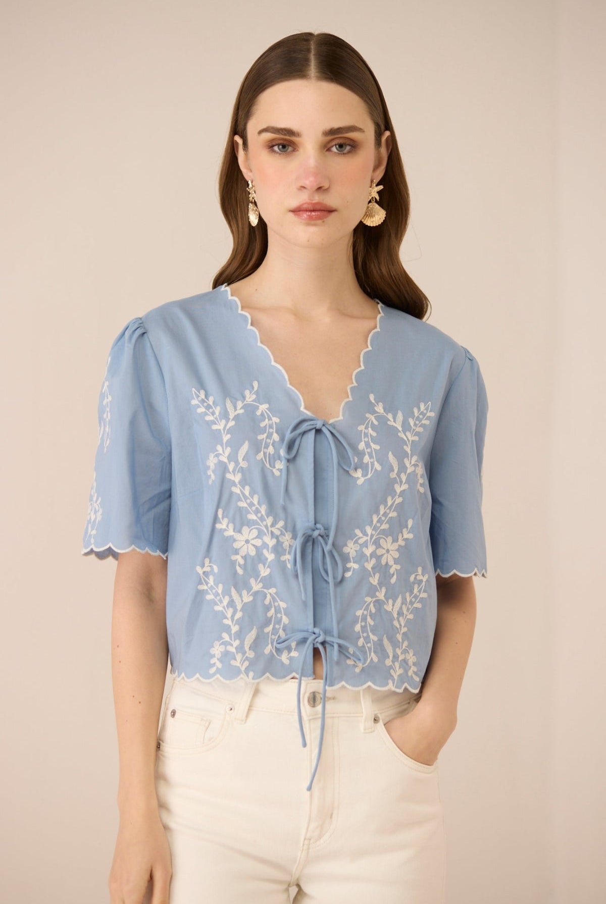 Woman wearing a light blue blouse with lace details on a beige background Calling June