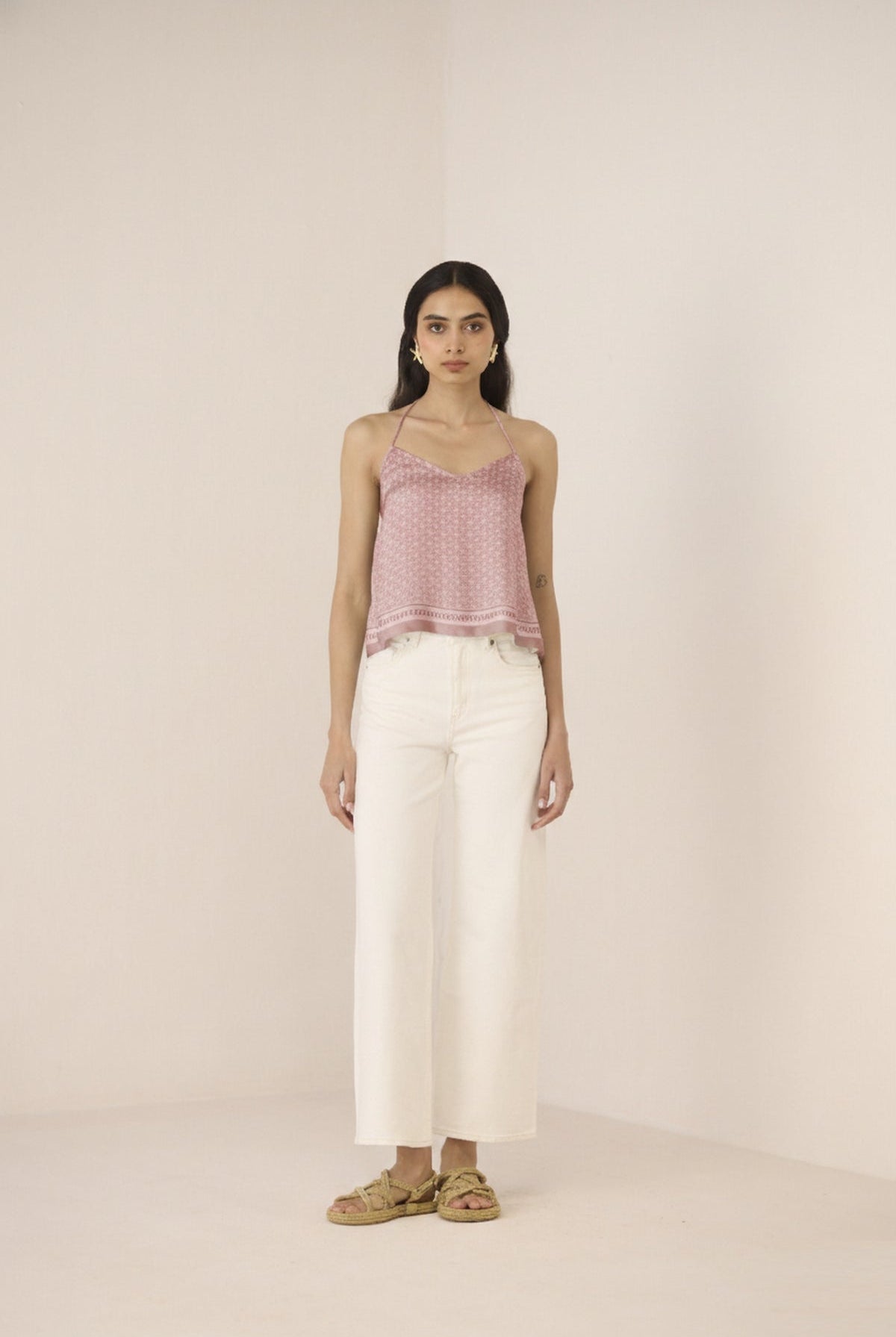 Woman wearing a pink top and white pants on a plain background Calling June