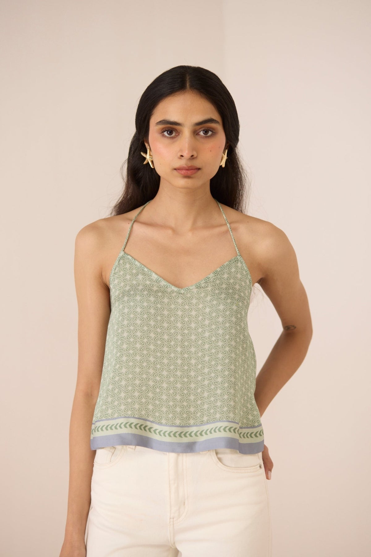 Woman wearing a green patterned top with white pants against a beige background Calling June