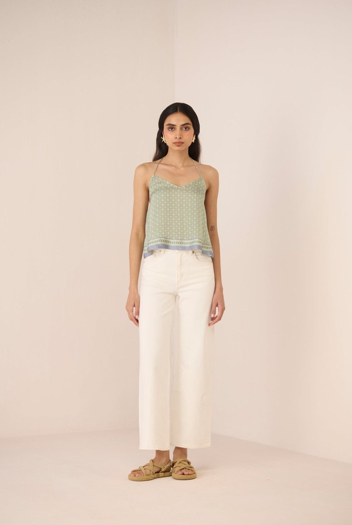 Woman wearing a green patterned top and white pants against a beige background Calling June