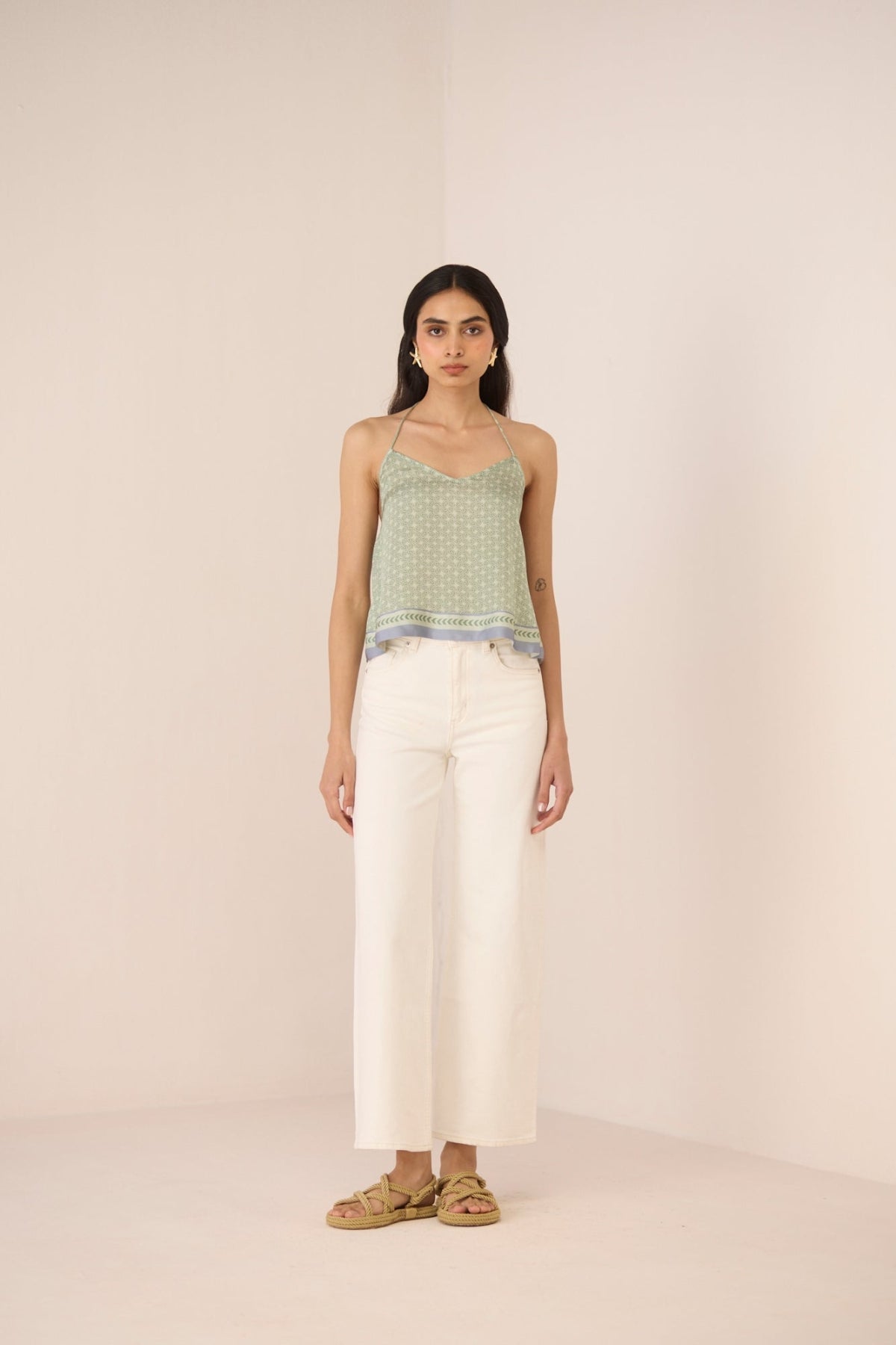 Woman wearing a green patterned top and white pants against a beige background Calling June