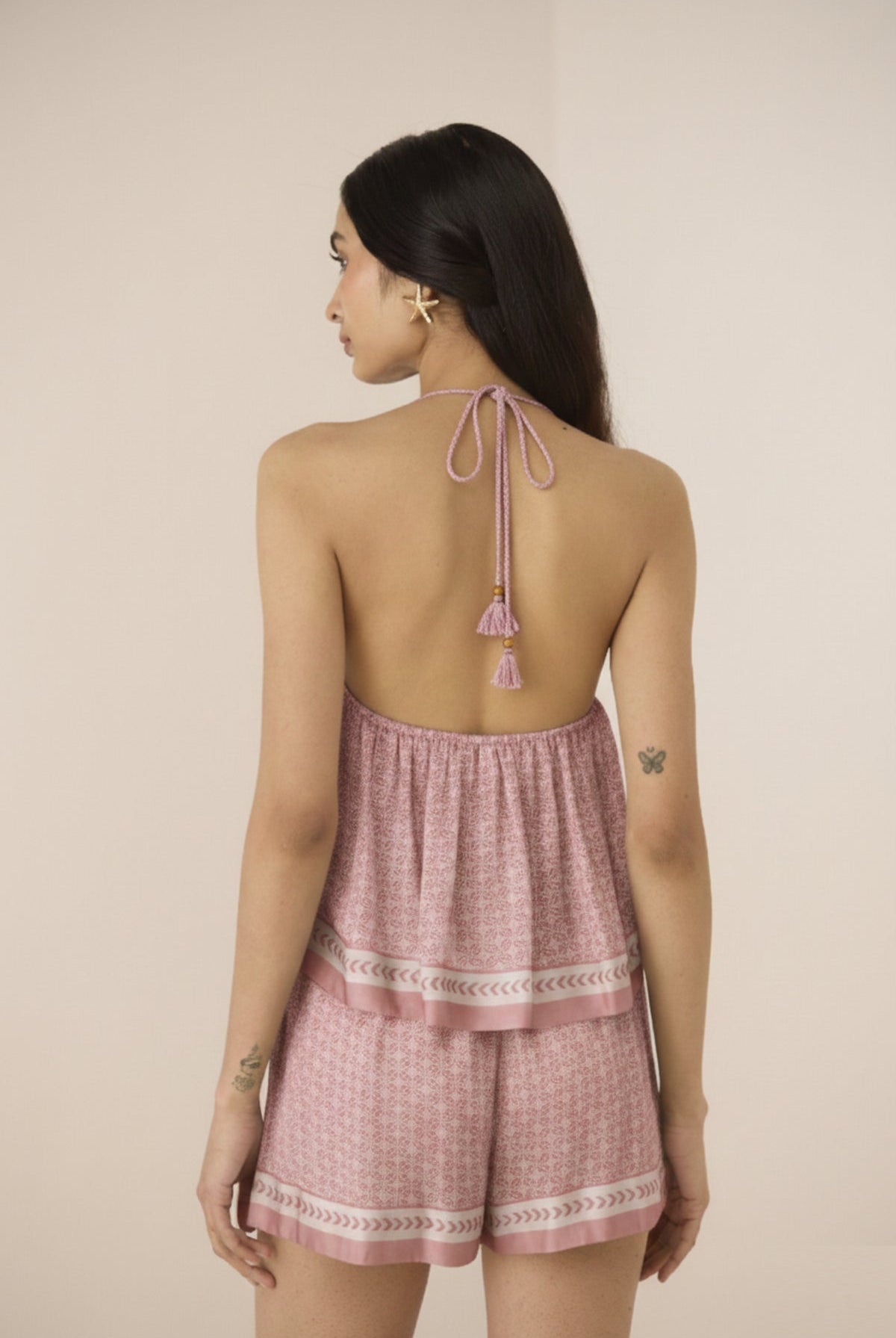Woman wearing a pink checkered romper with tassel details on a beige background Calling June