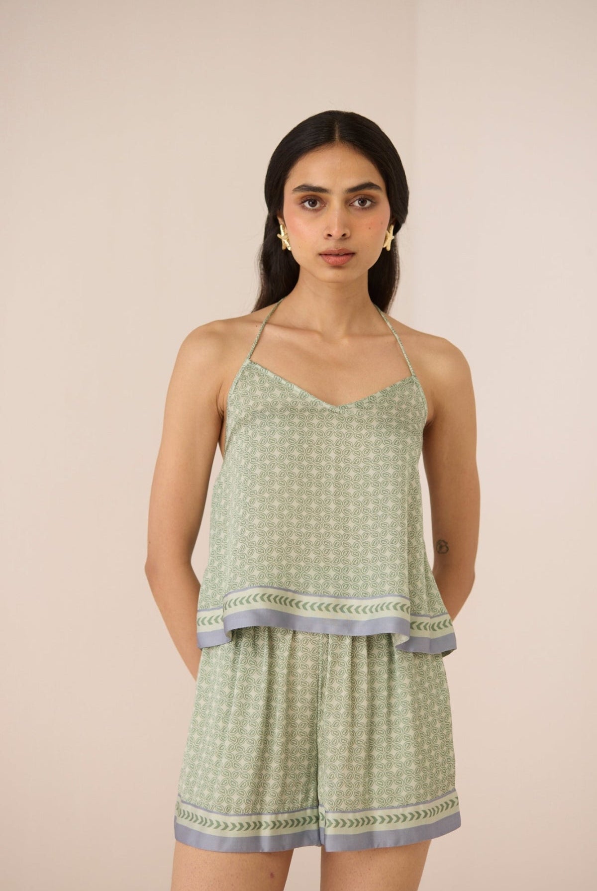 Woman wearing a green patterned top and shorts set on a beige background Calling June