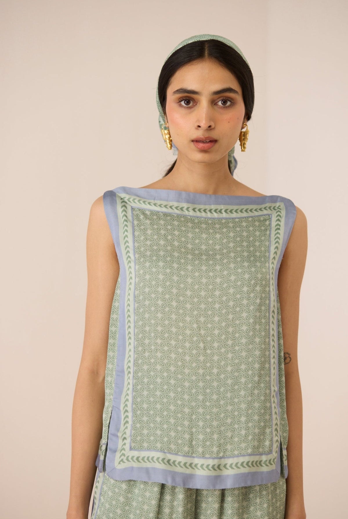 Woman wearing a green sleeveless top with a patterned border against a beige background Calling June