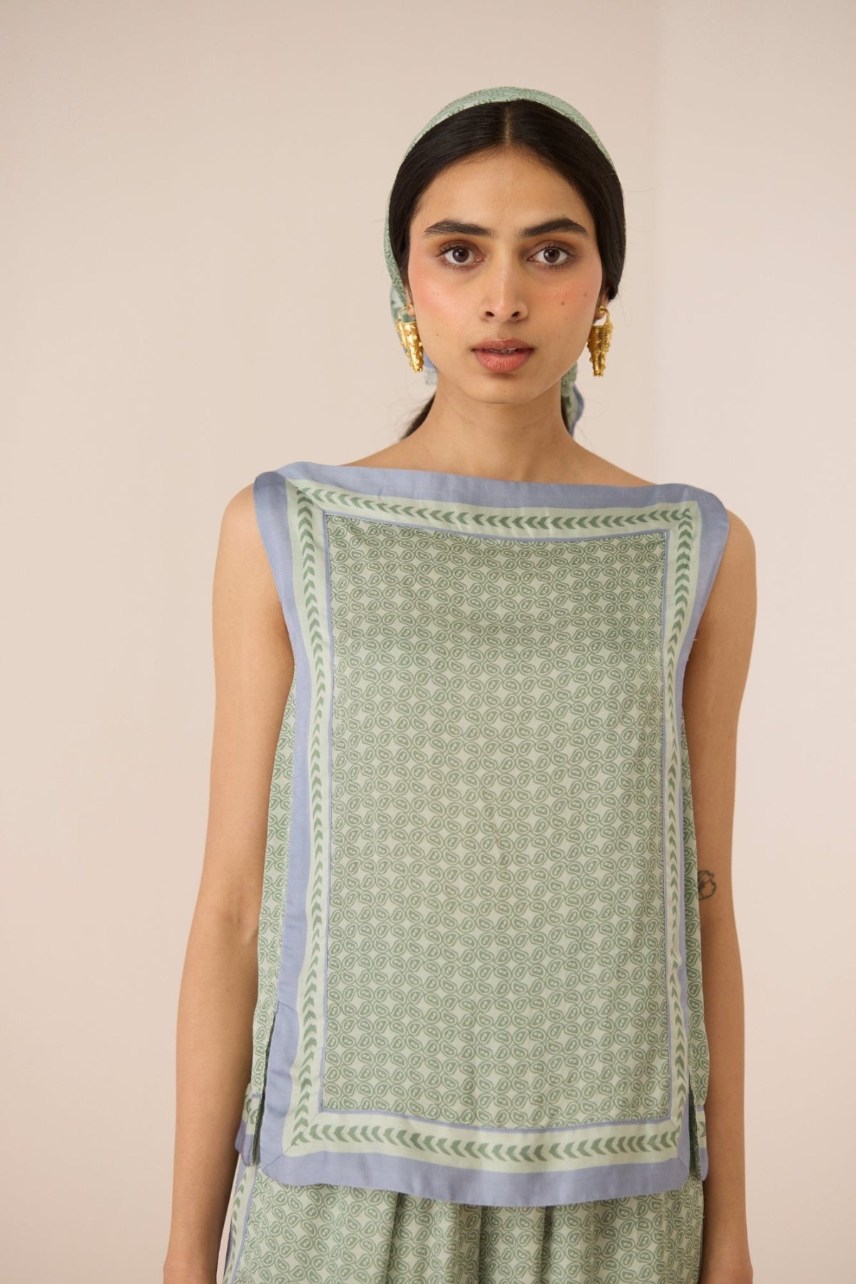 Woman wearing a green sleeveless top with a patterned border against a beige background Calling June