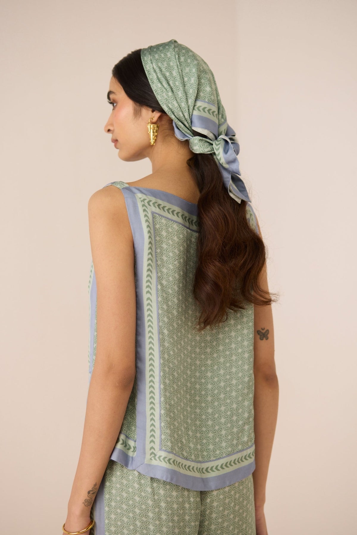 Woman wearing a green and white patterned top with a matching headscarf on a beige background Calling June