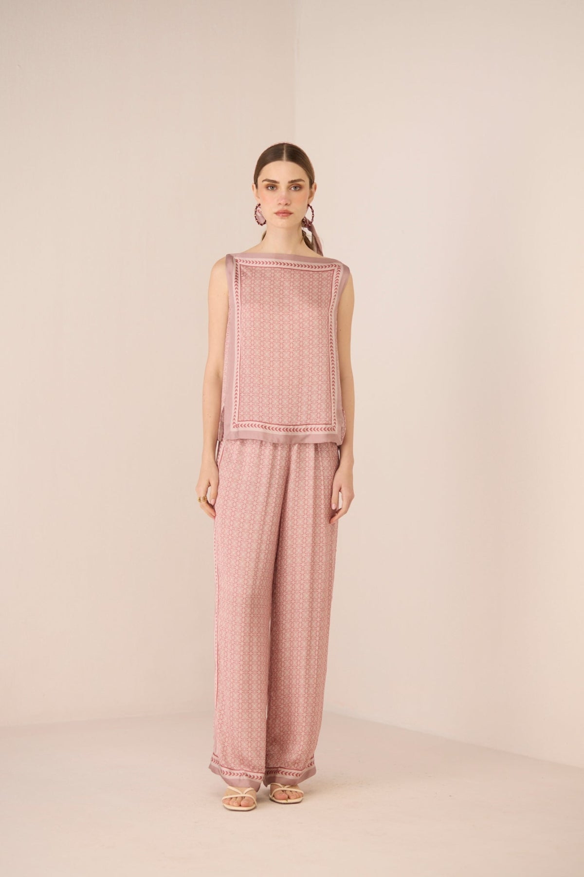 Woman wearing a pink textured sleeveless top and pants on a beige background Calling June