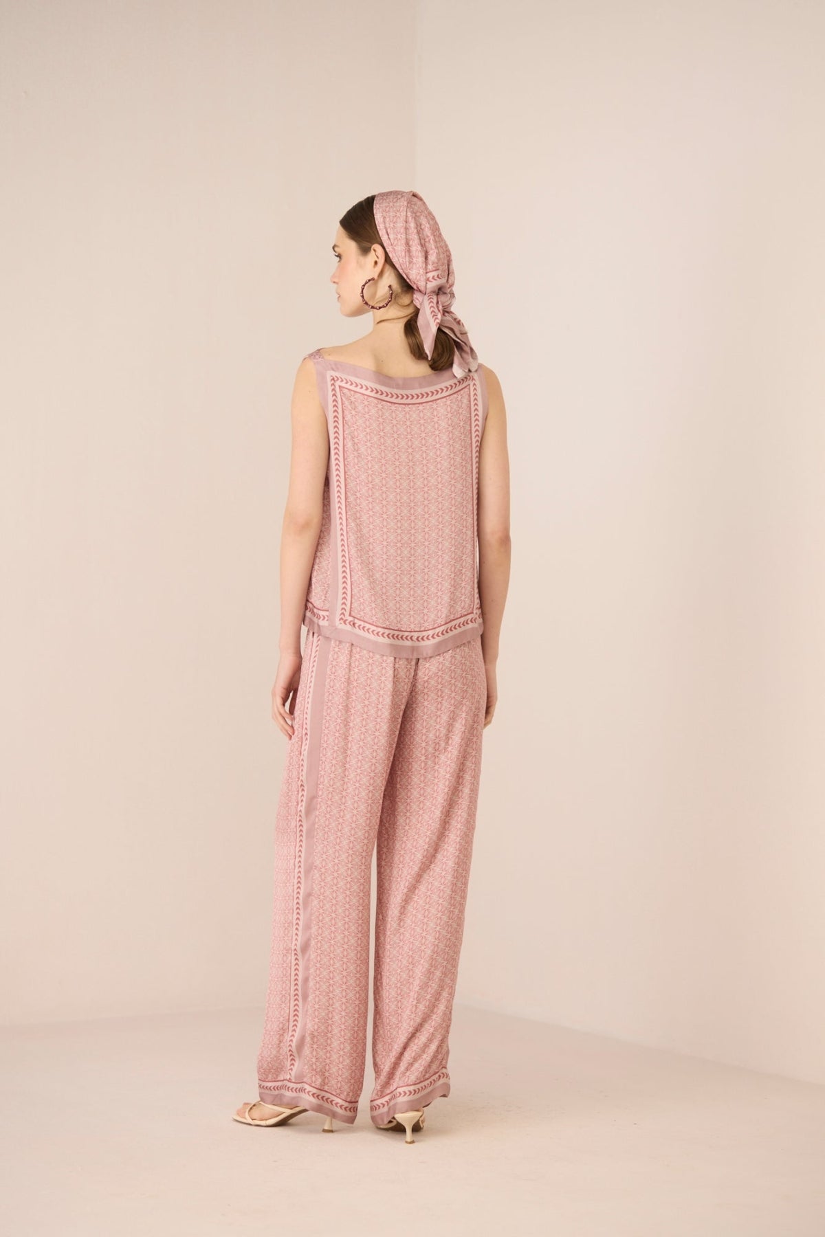 Woman wearing a pink textured jumpsuit with a matching headscarf on a beige background Calling June